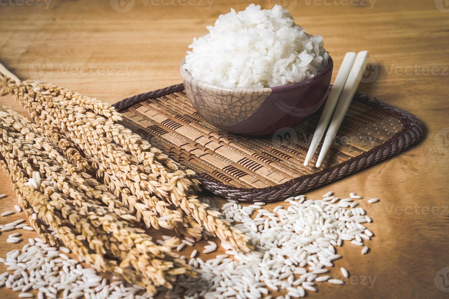 Cooked rice in bowl with raw rice grain and dry rice plant on  wooden table background. photo