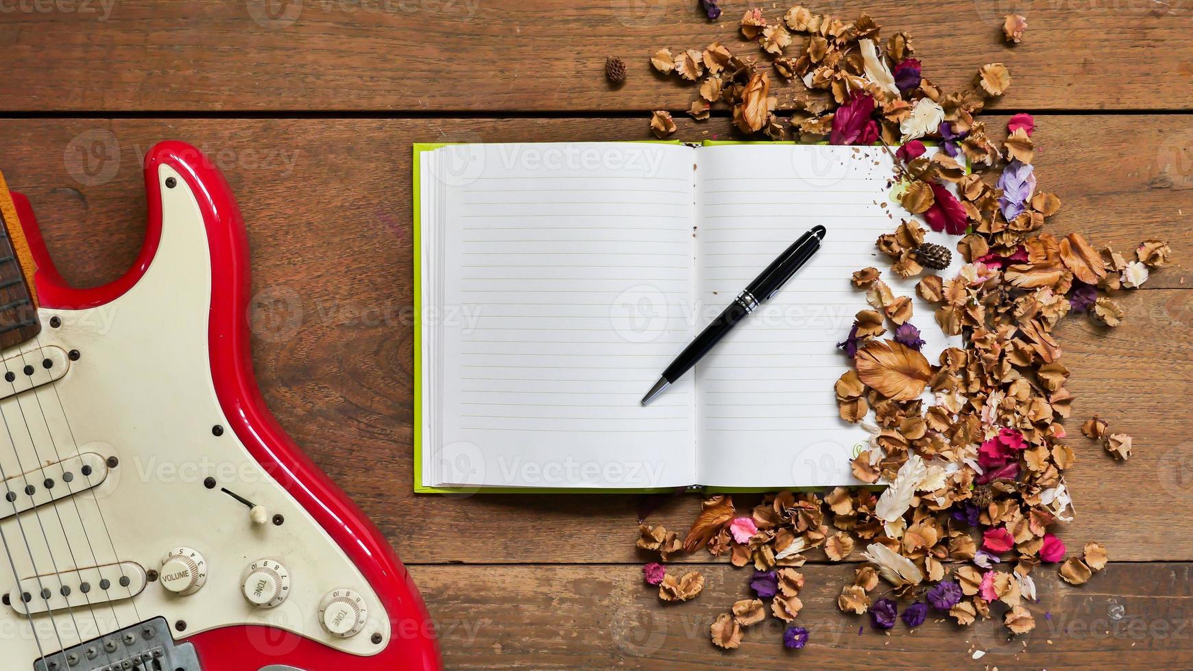 Top view workspace with notebook,pen,electric guitar  and dried flowers on wooden table background . photo