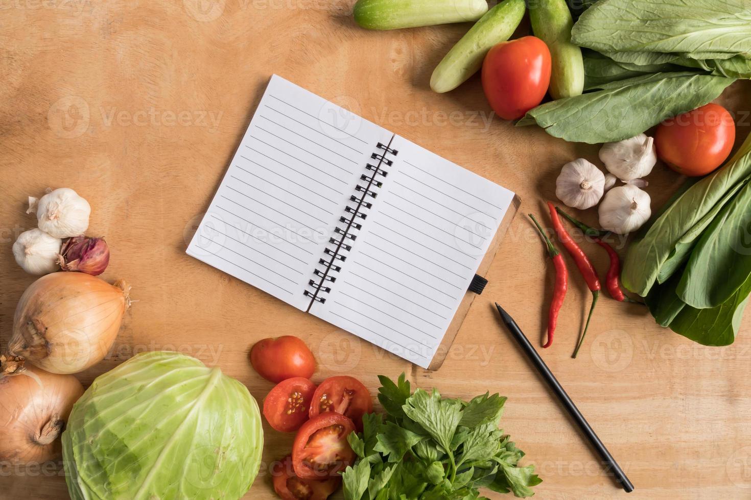 vista superior de verduras frescas con cuaderno en blanco sobre fondo de mesa de madera. foto