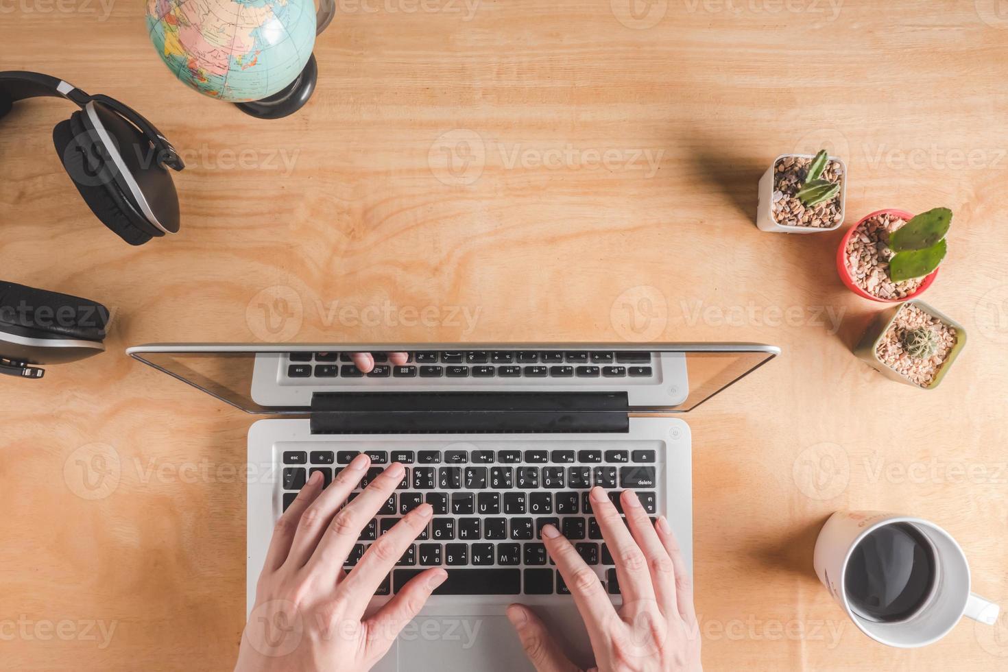 Topview of Male hands woking on laptop with headphone ,cactus,globe and coffee cup on wooden table background. photo