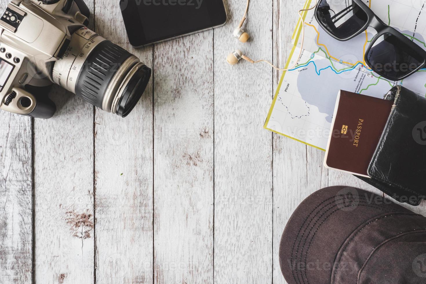 vista superior de la cámara con gorra, gafas de sol, billetera, teléfono inteligente, mapa y pasaporte sobre fondo de mesa de madera blanca, concepto de viaje foto