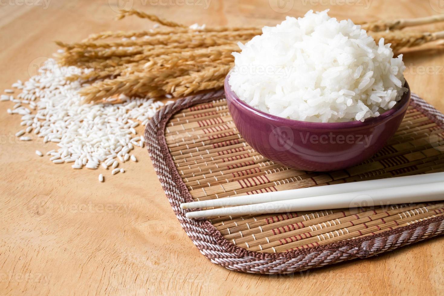 Cooked rice in bowl with raw rice grain and dry rice plant on  wooden table background. photo