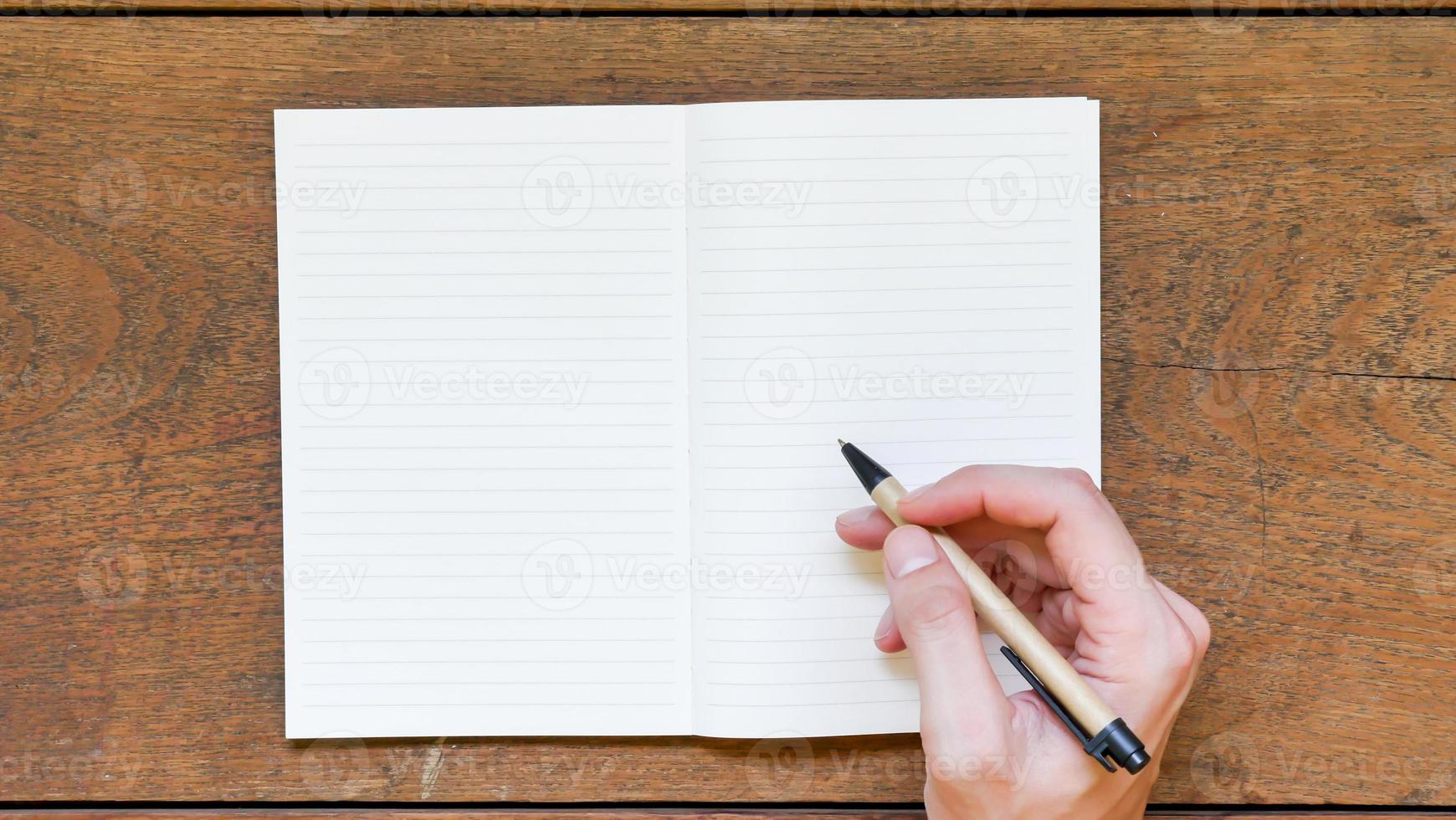 Man hands with pen writing on empty notepad over wooden table. photo