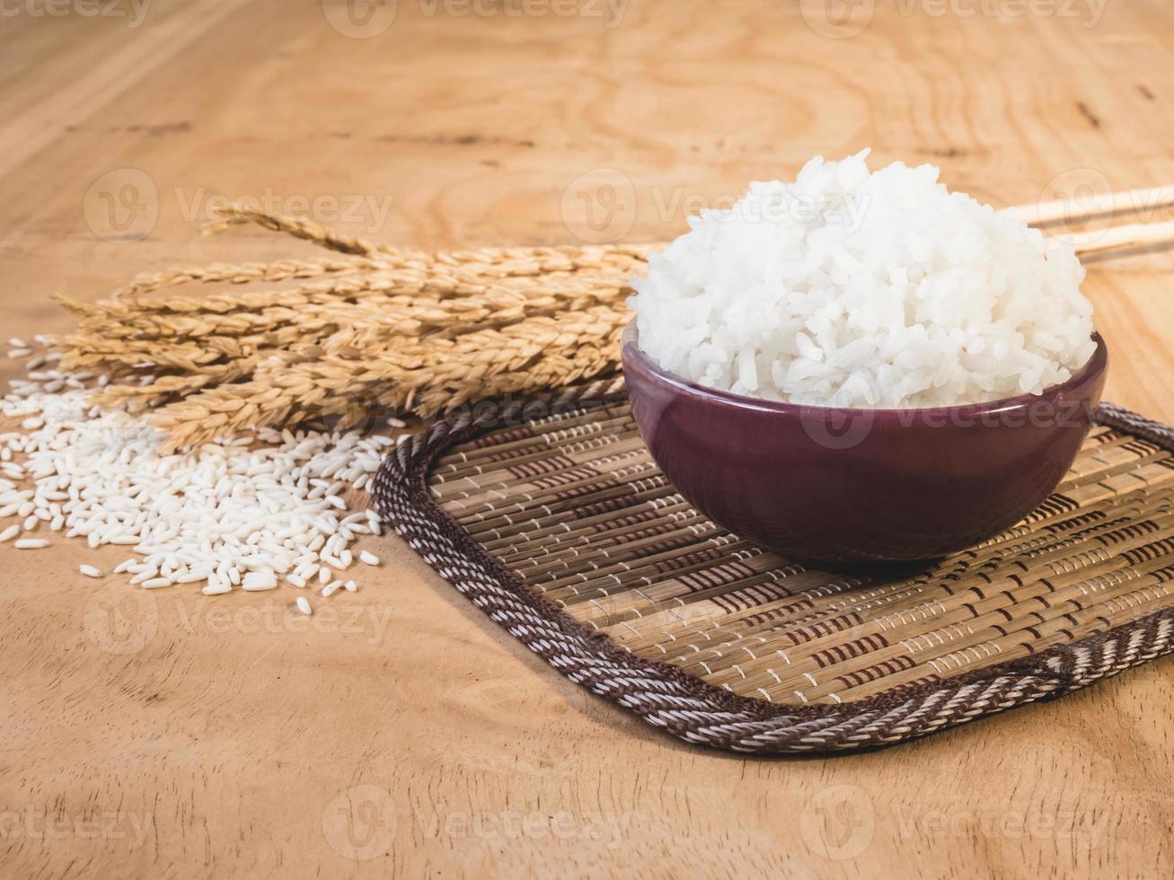 arroz cocido en tazón con grano de arroz crudo y planta de arroz seco sobre fondo de mesa de madera. foto