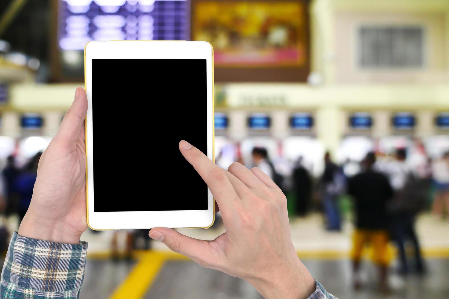 Male hands holding a white tablet with touch blank black screen on blurred image of people buy ticket at the counter background. photo