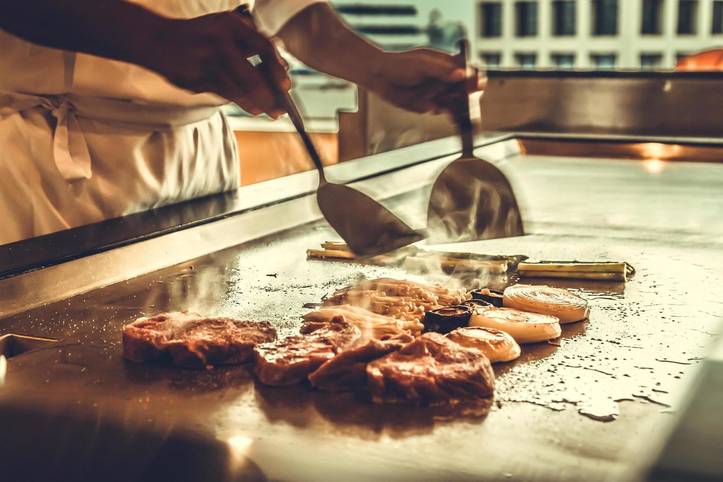 cerrar las manos chef cocinando bistec de ternera y verduras en una sartén caliente, comida japonesa foto