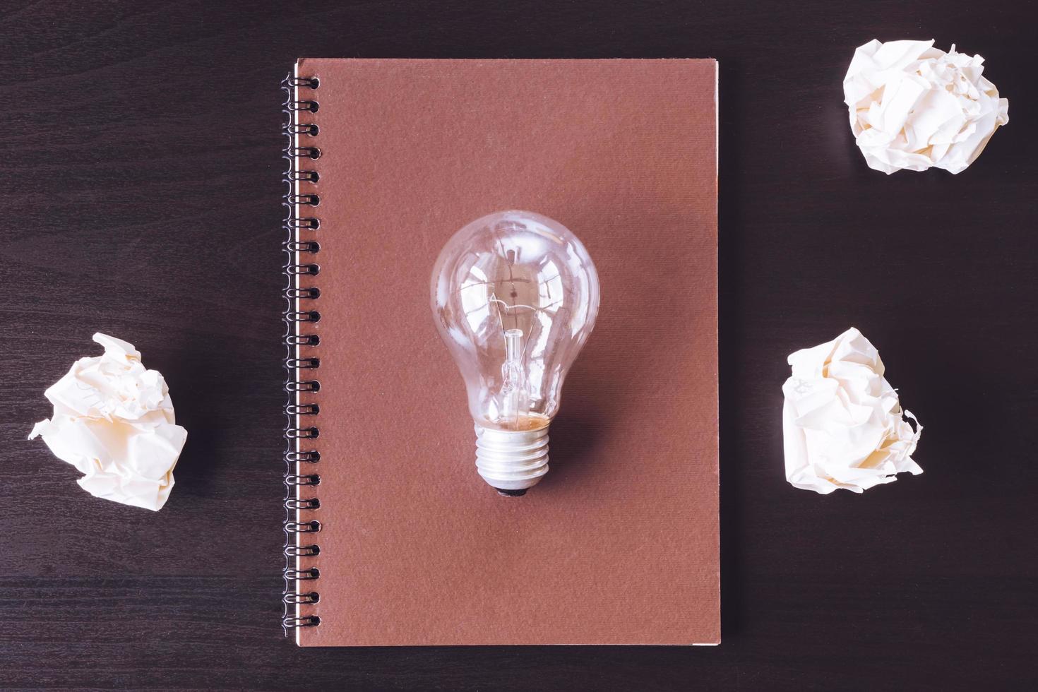 Top view notebook with crumpled paper balls and light bulb on the desk. photo