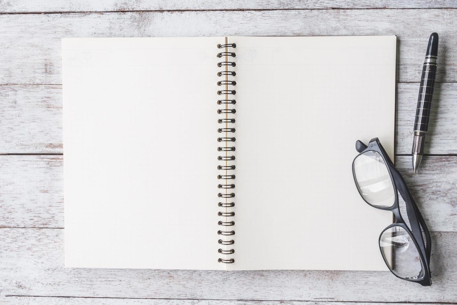 Top view of Notebook with pen and glasses on white wooden table background. photo