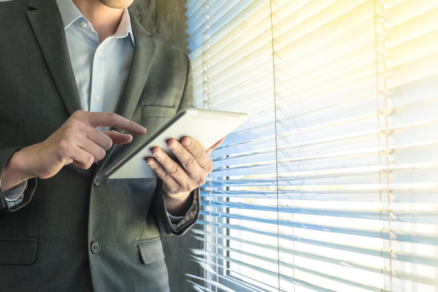Close up of businessman using tablet device while standing at a window in an office photo