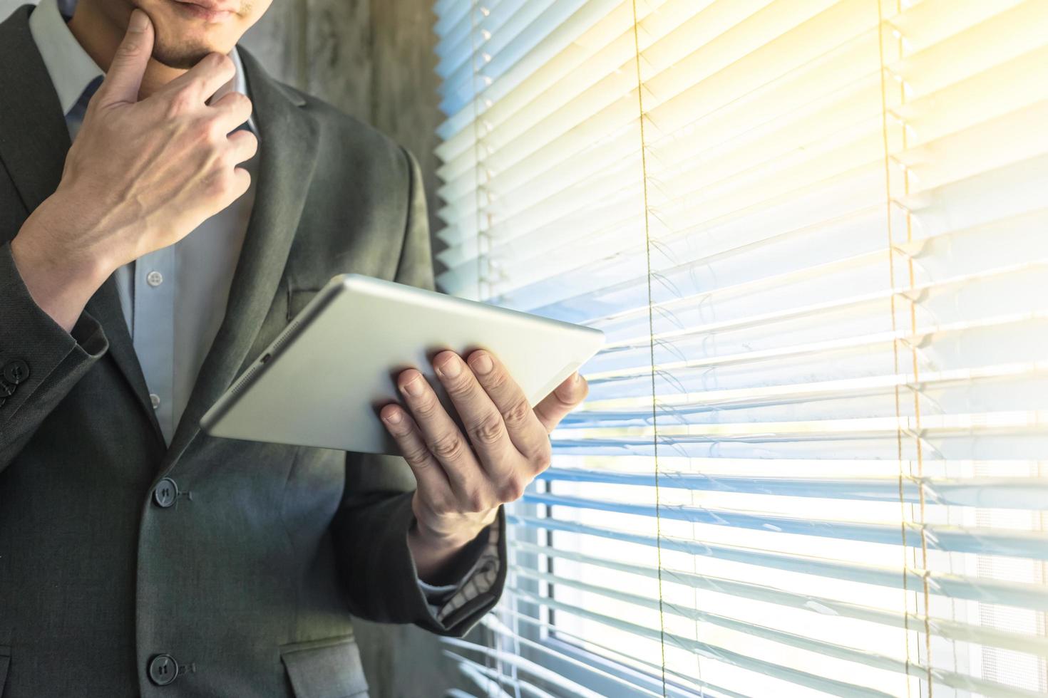 Close up of businessman using tablet device while standing at a window in an office photo