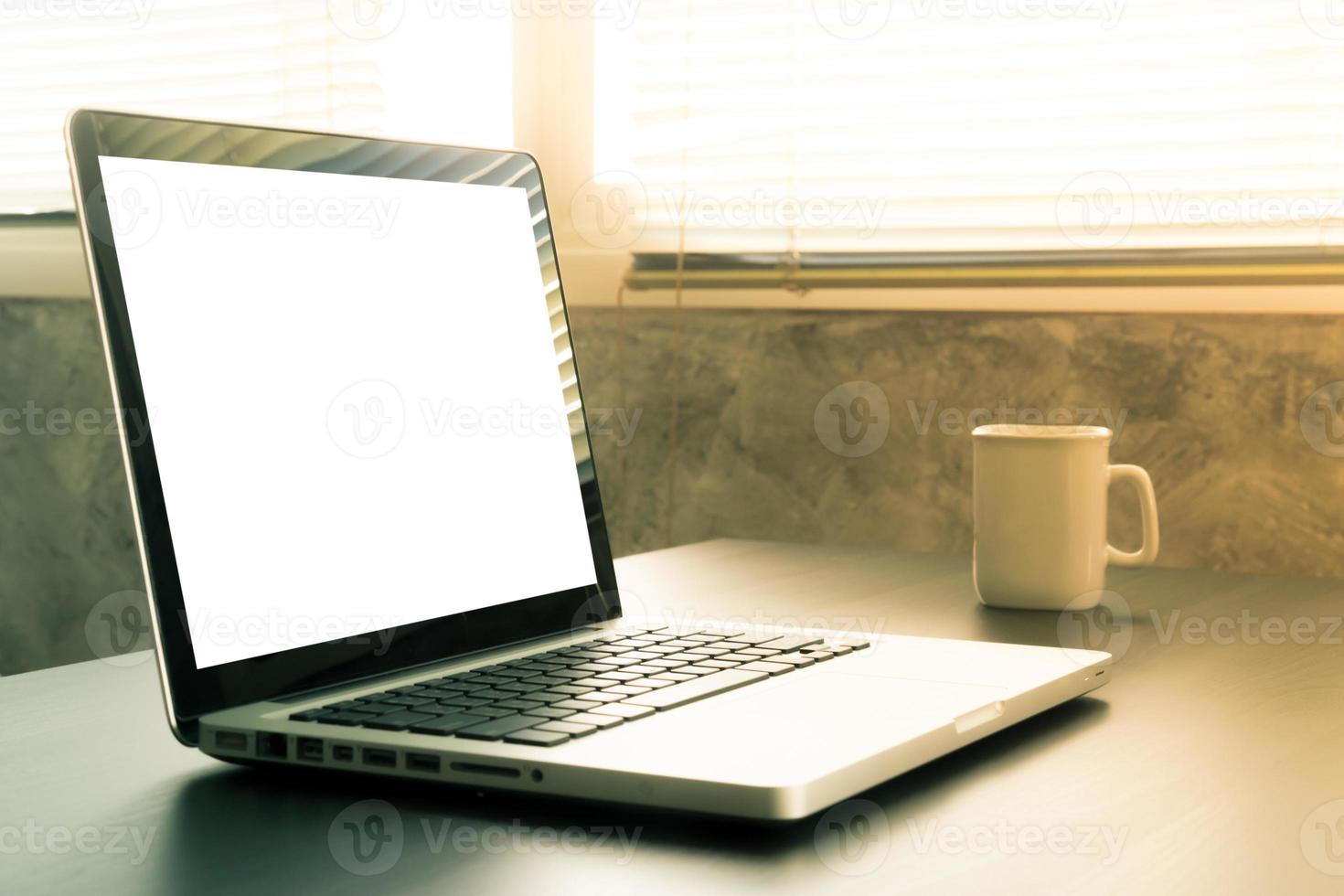 Laptop with white blank screen, white cup of coffee on the desk, Vintage tone photo