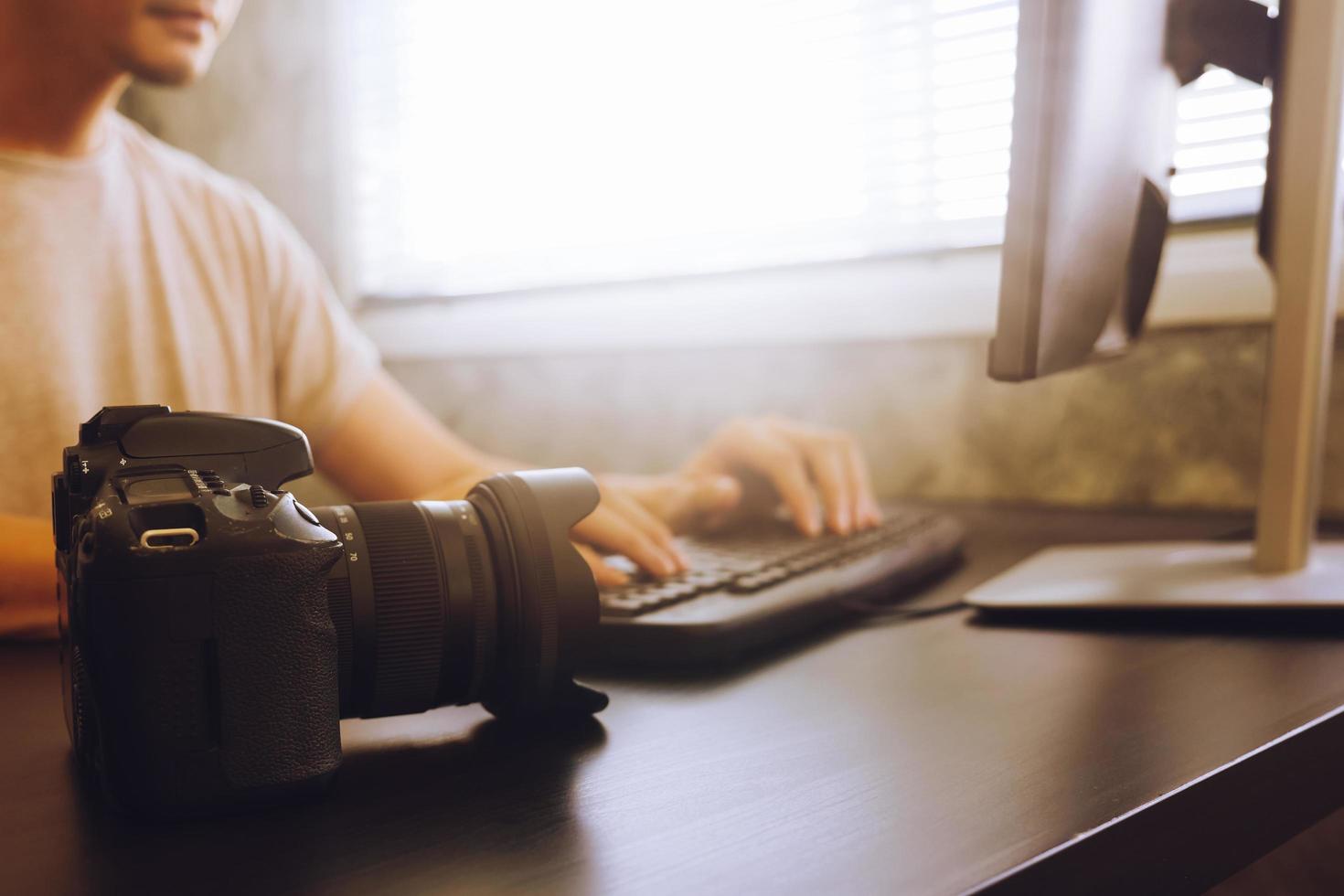 Casual young man working on computer with camera, sitting at desk, toned with sunlight photo