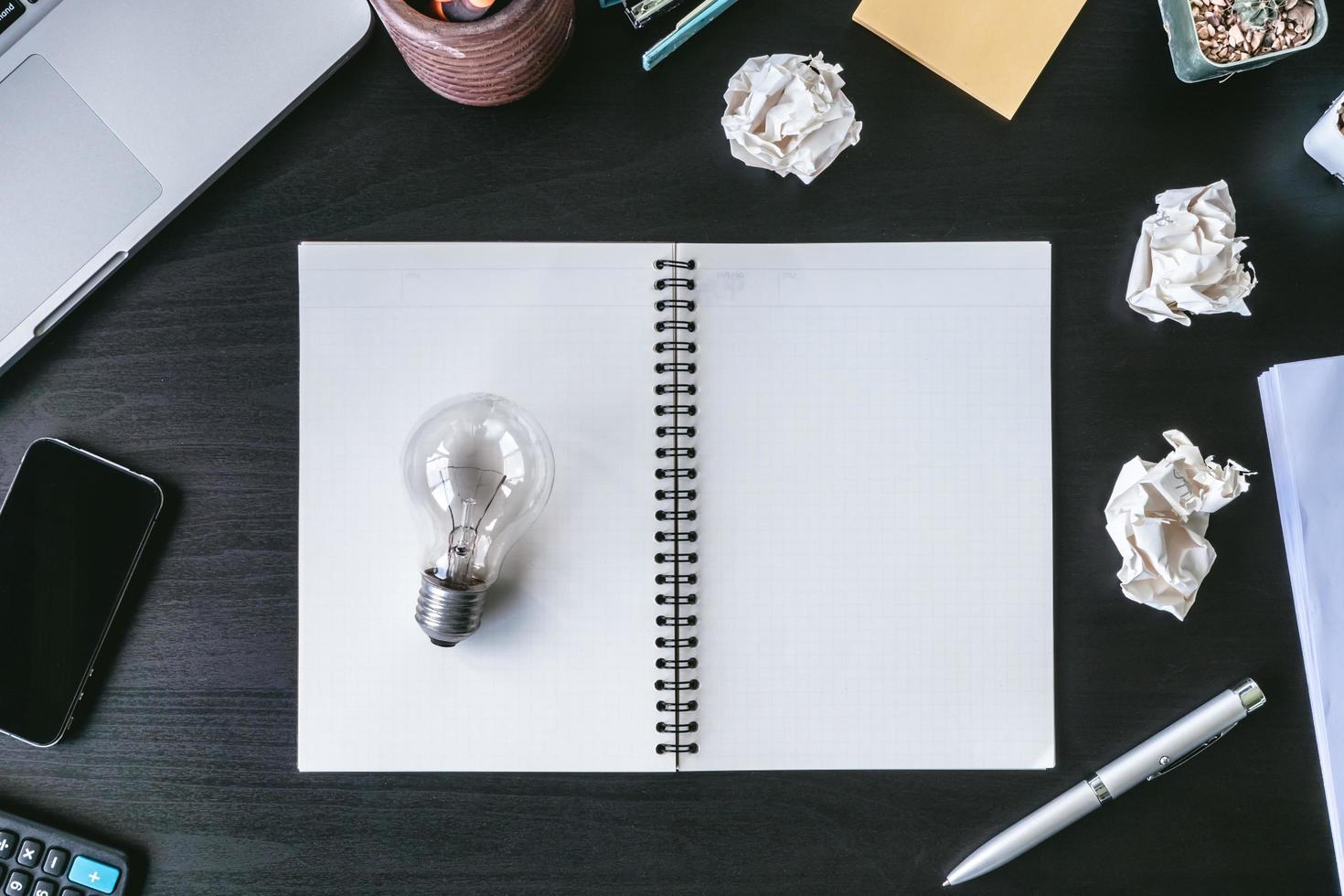 Top view notebook with crumpled paper balls and light bulb on the desk. photo