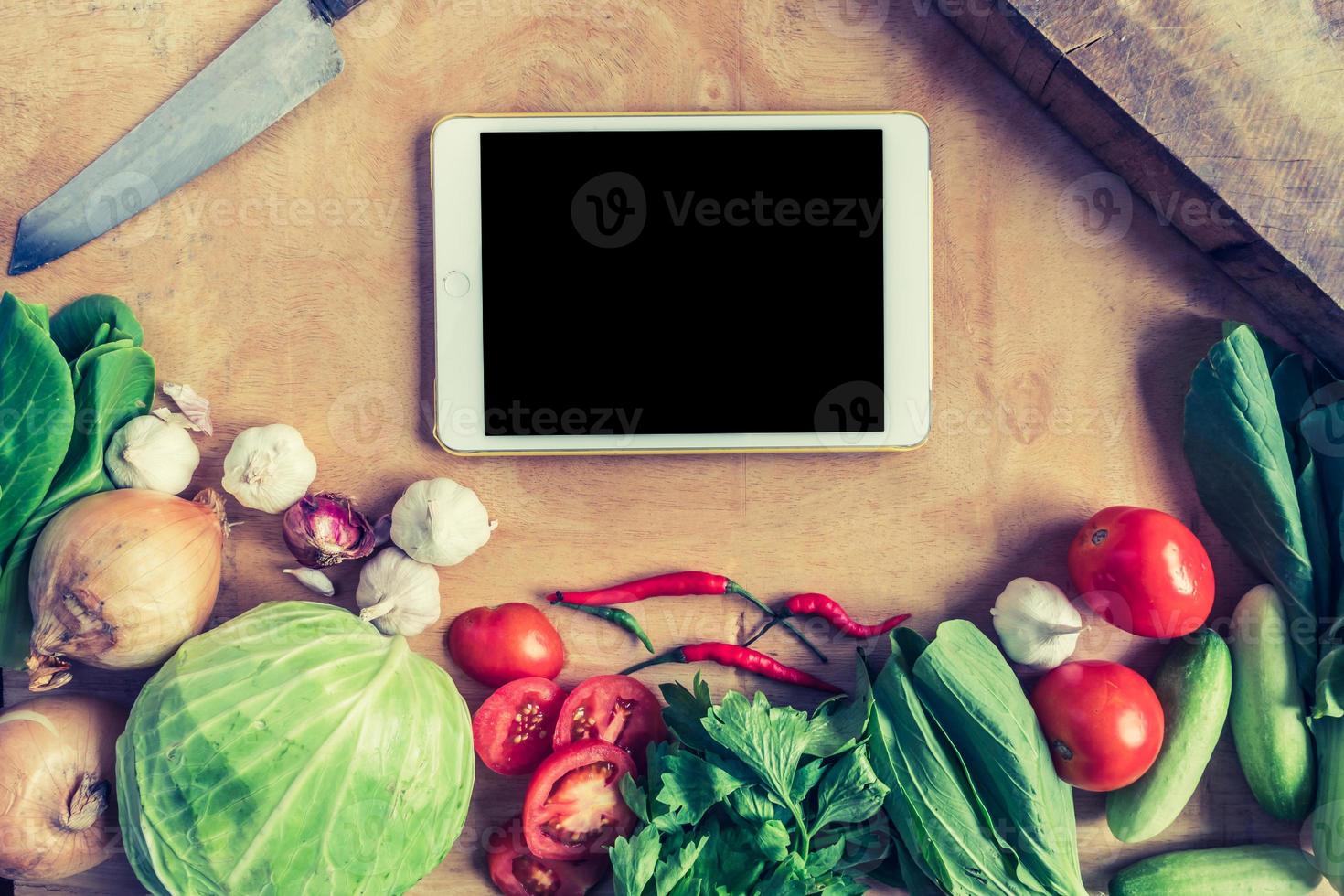 Top view of Fresh vegetables with tablet touch computer gadget on wooden table background. photo