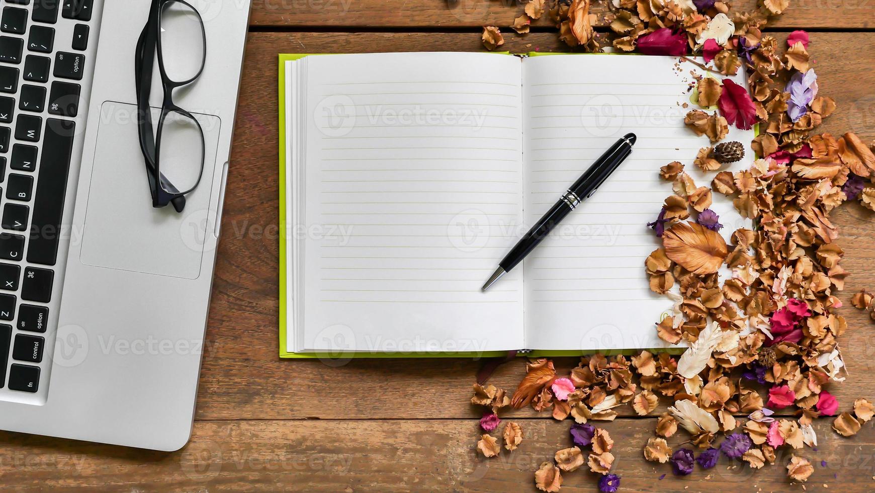 Top view workspace with notebook,pen,glasses,laptop and dried flowers on wooden table background . photo