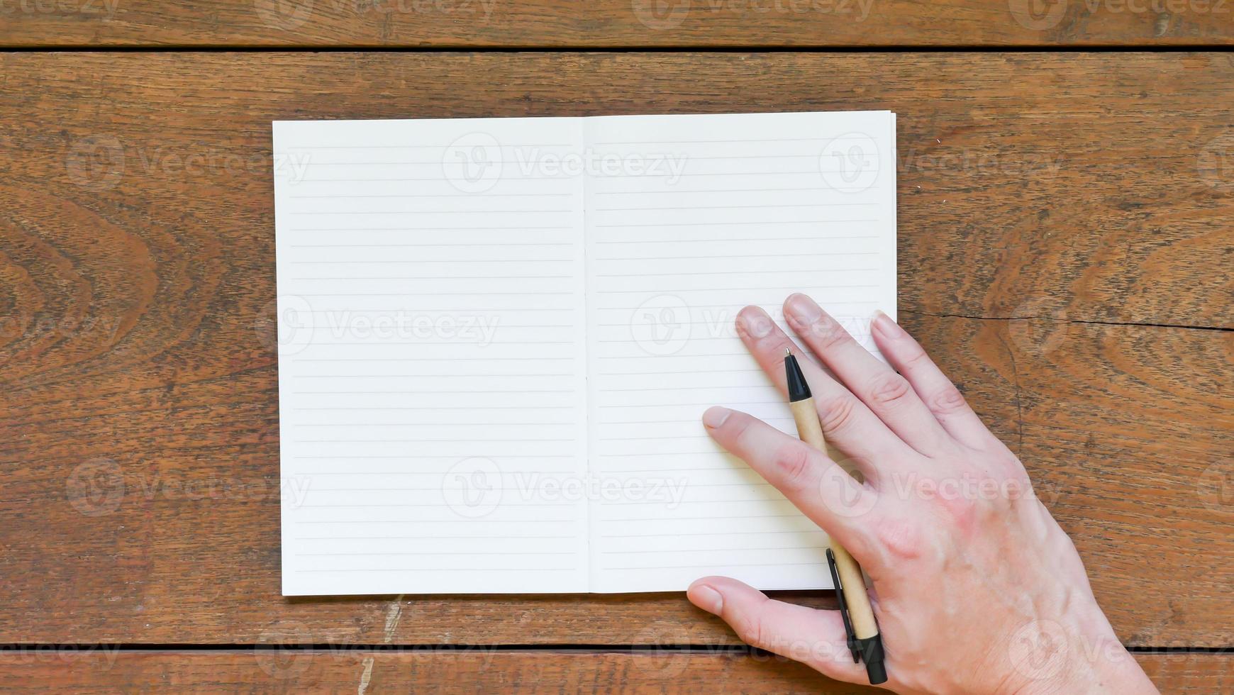 Man hands with pen writing on empty notepad over wooden table. photo