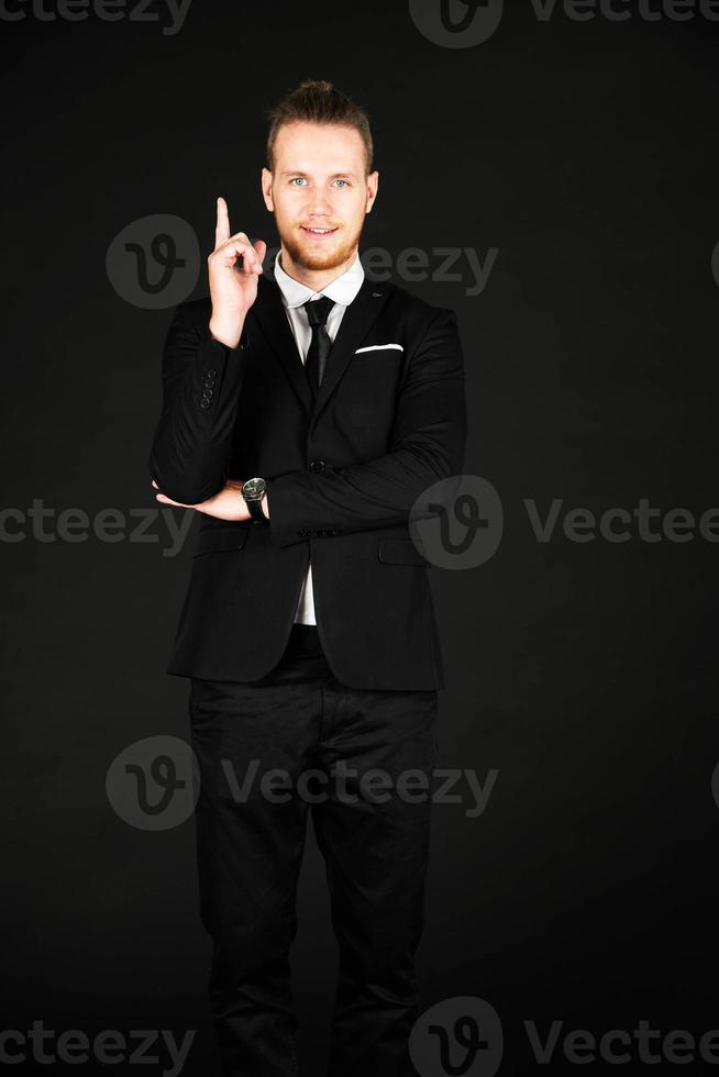 Portrait of handsome businessman in black suit showing okay symbol hand isolated on black background photo
