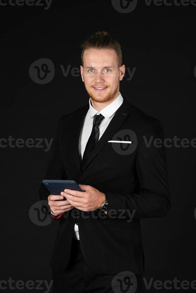 Portrait of handsome businessman in black suit holding and working with tablet isolated on black background photo