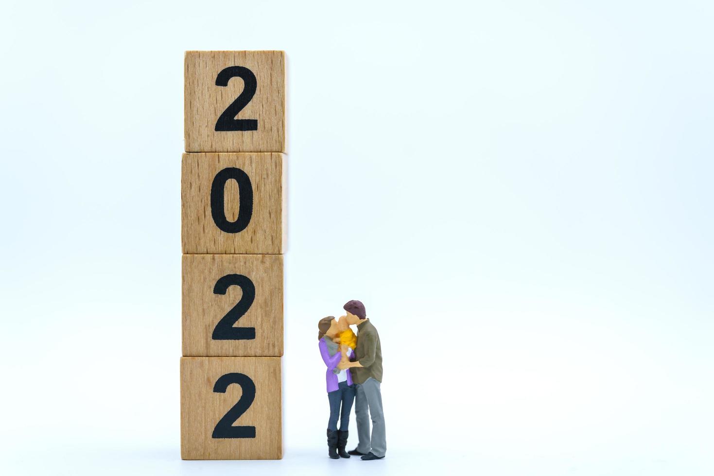 2022 New Year and Family Concept. Closeup of parent and child miniature figures hug and kissing with stack of wooden number block on white background. photo