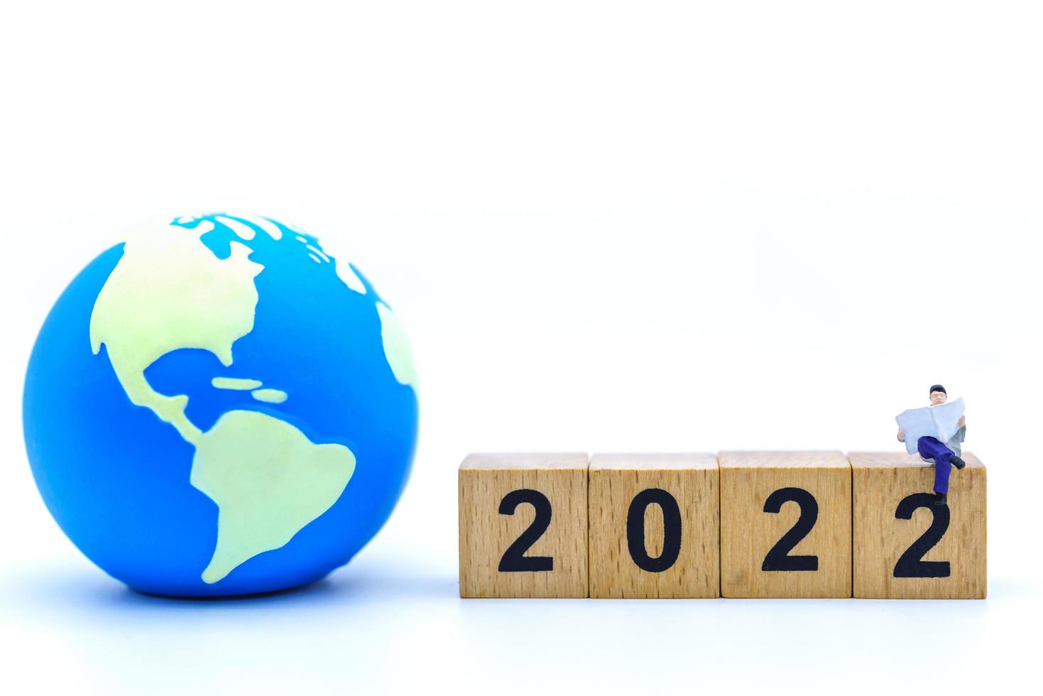 2022 New Year and Business Concept. Closeup of businessman miniature figures sitting and reading a book or newspaper on wooden number block with mini world ball on white background. photo