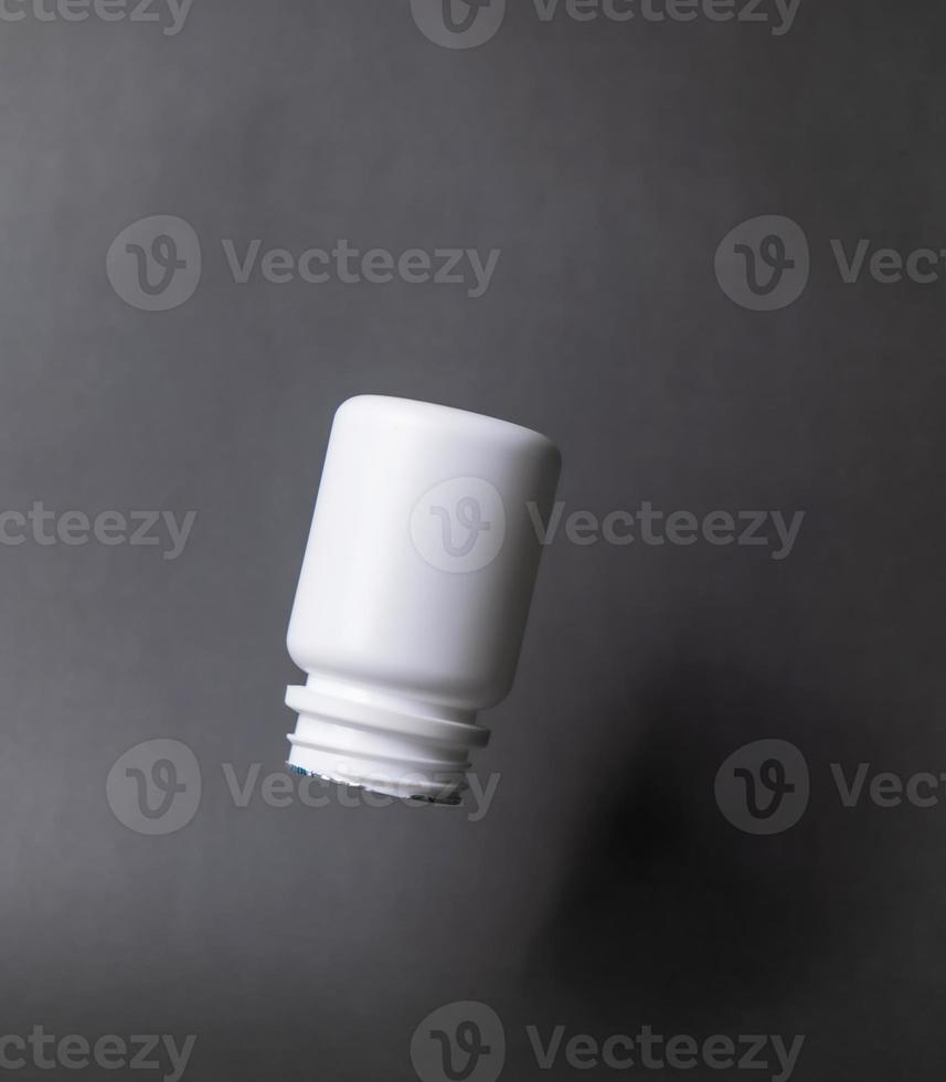 White plastic pill bottle, unlabelled, open cap. come out below in black background photo