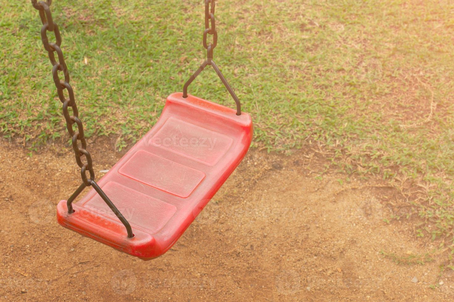 A red swing is attached to a rusty old chain in the playground. in the park saw the ground and the grass photo