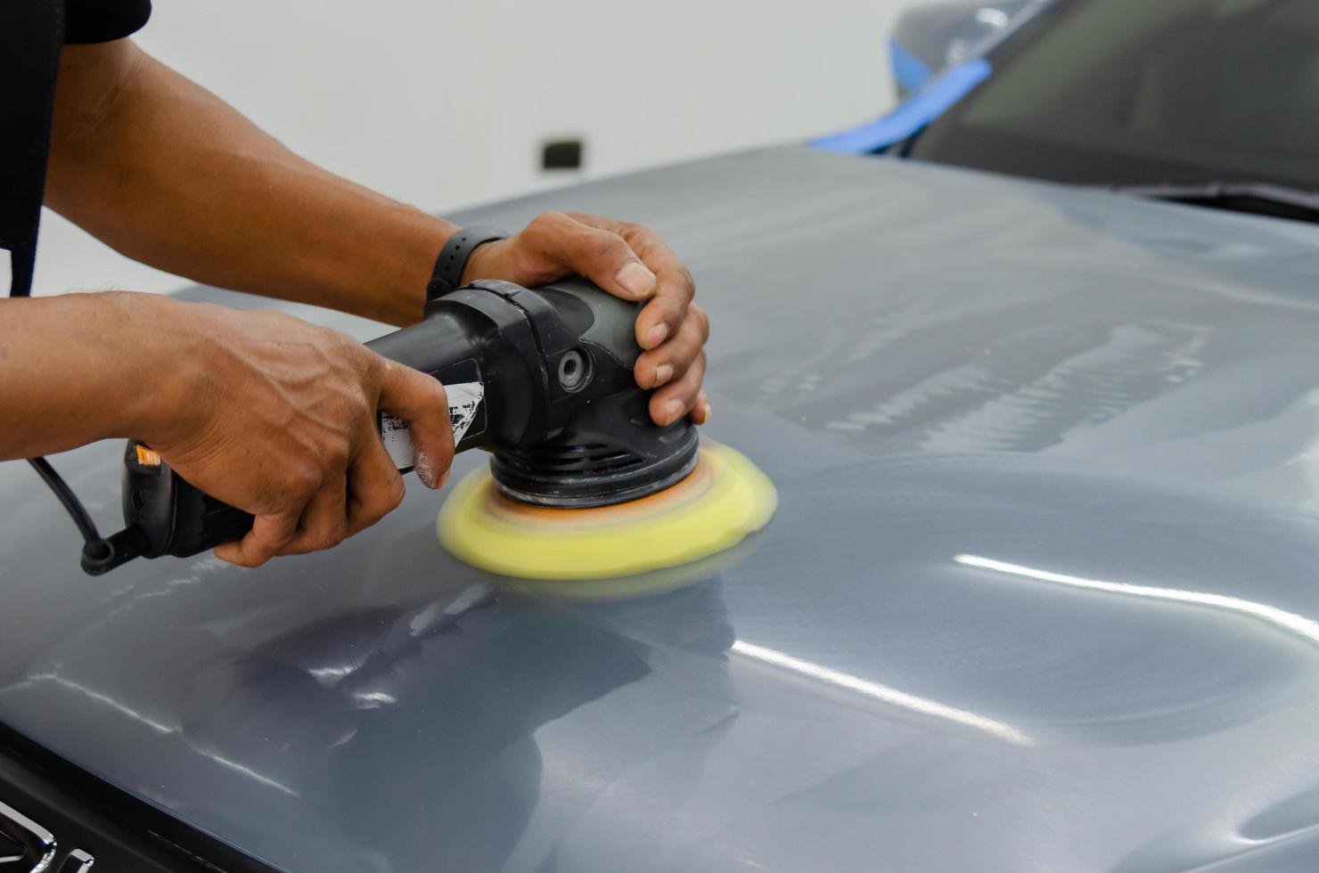 hombre que sostiene la herramienta pulido mecánico reparación de automóviles que detalla el mantenimiento del rasguño del automóvil del capó en el trabajo de lavado de autos en el garaje. foto