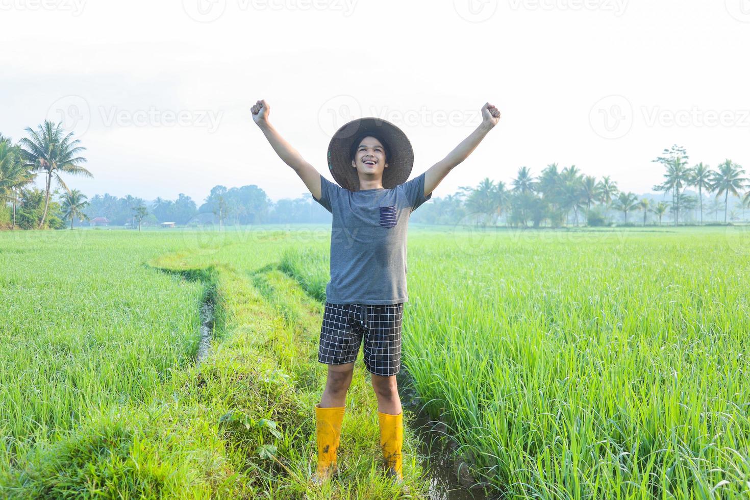 joven agricultor milenario asiático de pie y sonriendo se siente orgulloso del éxito del cultivo de arroz con cáscara en el campo de arroz. concepto de agricultura moderna. foto