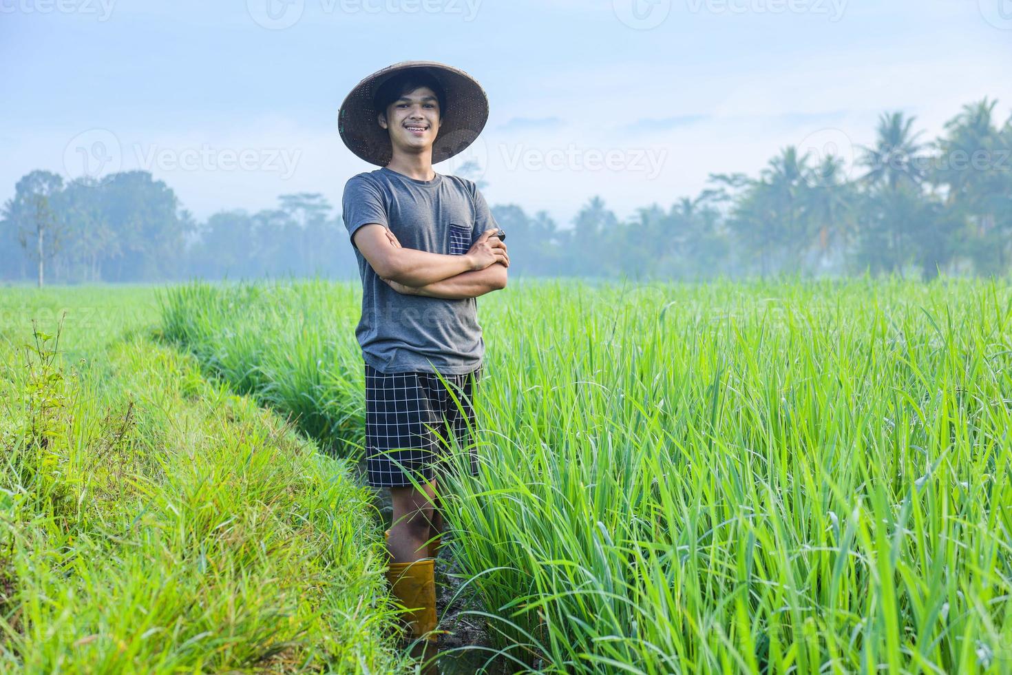 Attractive cheerful young Asian farmer standing, smiling and confident showing success to growing paddy rice in the rice field. Modern agriculture concept. photo