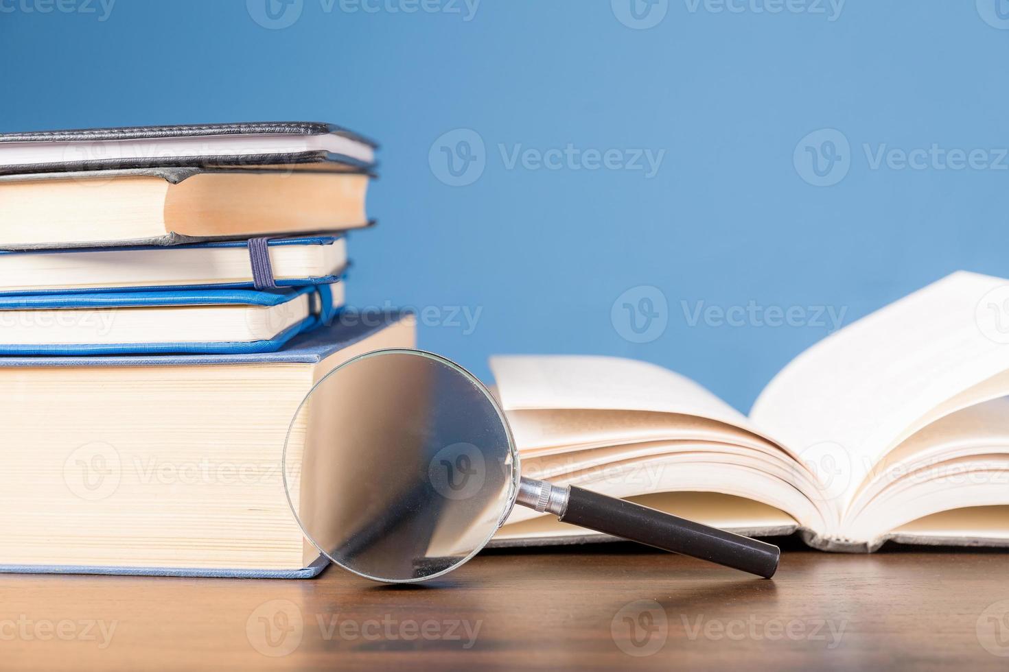 Stack book with magnifying glass on wooden desk in information library of school or university, concept for education, reading, study, copy space on blue background. photo