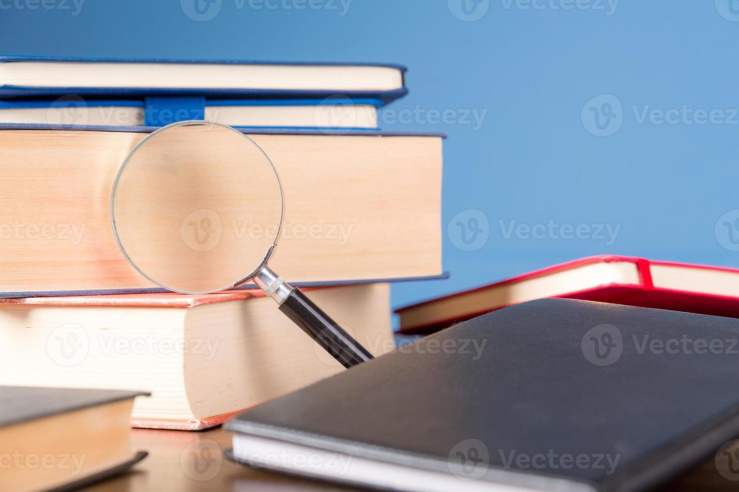 Stack book with magnifying glass on wooden desk in information library of school or university, concept for education, reading, study, copy space on blue background. photo