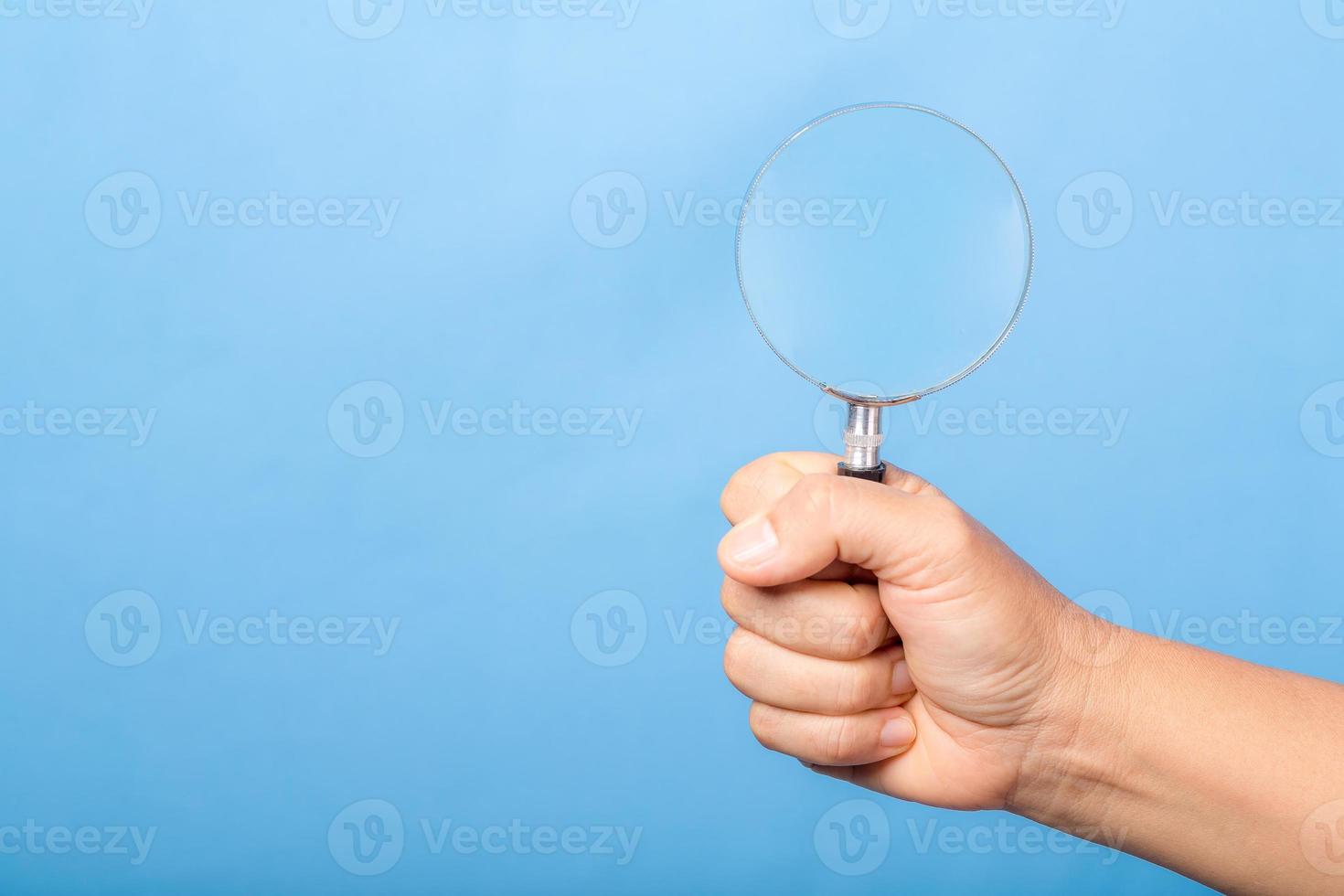 woman hand holding magnifying glass isolated on blue background. optical zoom lens is macro tool, concept for education, science. photo