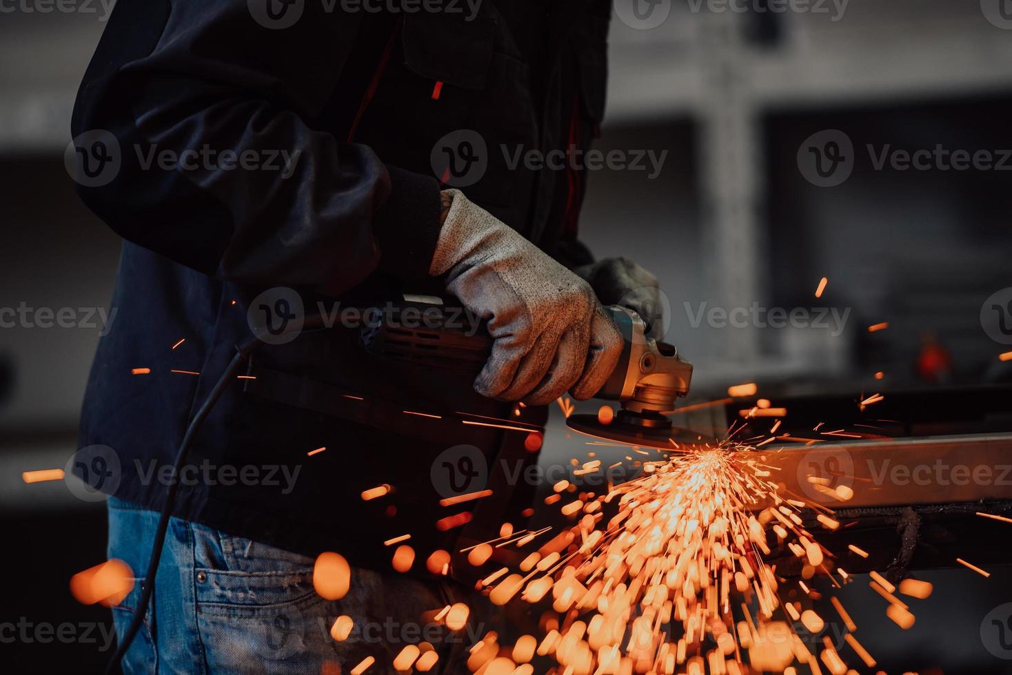 interior de fábrica de ingeniería de industria pesada con trabajador industrial usando amoladora angular y cortando un tubo de metal. contratista en estructuras metálicas de fabricación de cascos y uniformes de seguridad. foto