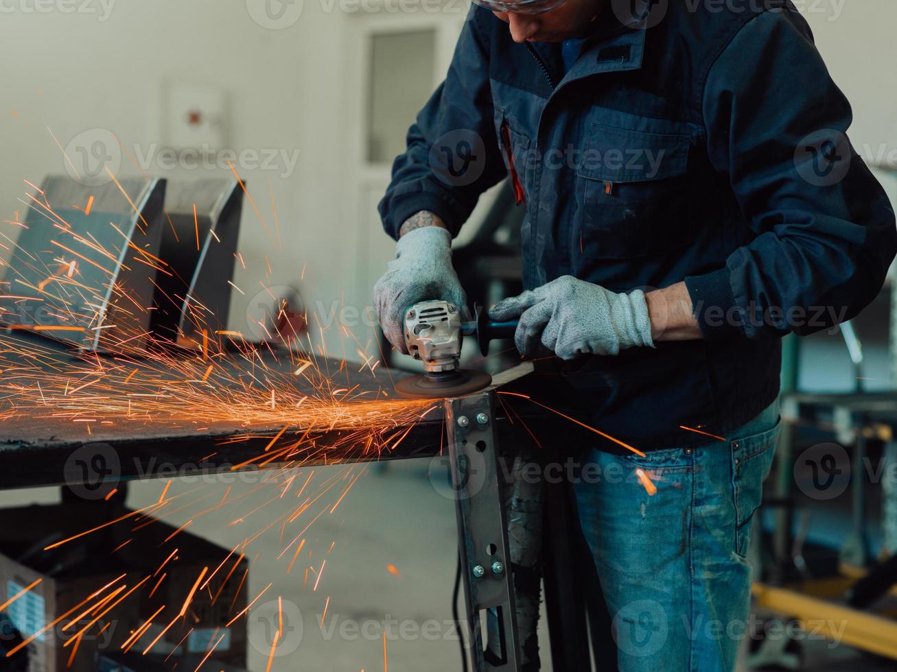 Heavy Industry Engineering Factory Interior with Industrial Worker Using Angle Grinder and Cutting a Metal Tube. Contractor in Safety Uniform and Hard Hat Manufacturing Metal Structures. photo