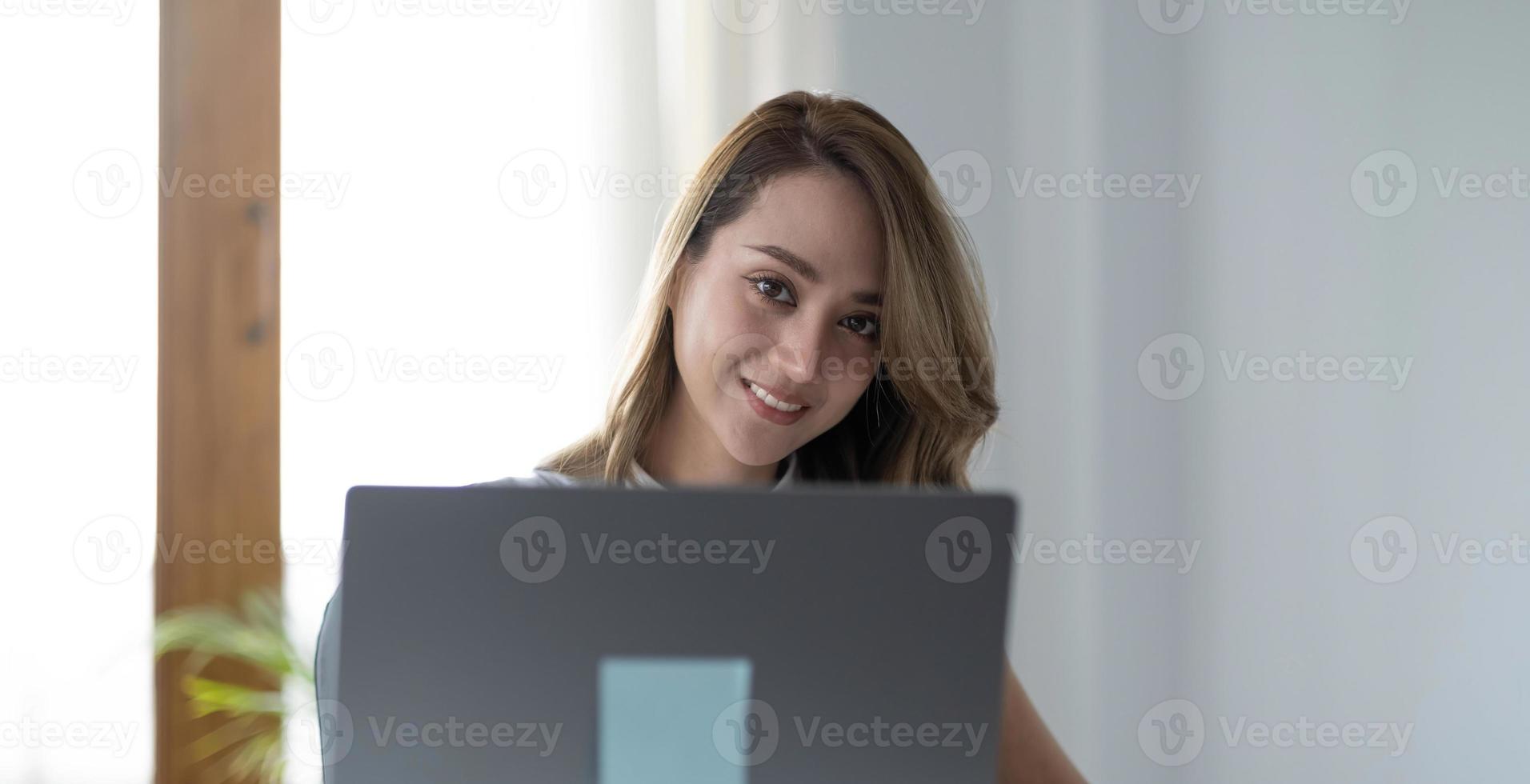 encantadora mujer asiática que trabaja en la oficina usando una laptop mirando la cámara. foto