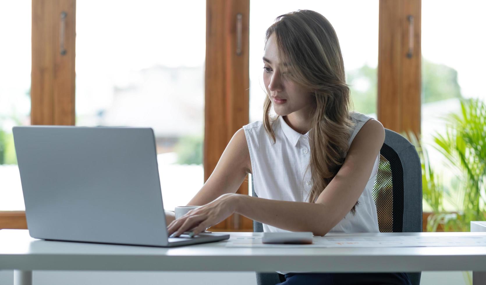 Front view of a beautiful Asian businesswoman working on a tablet coffee cup placed on the office table. photo