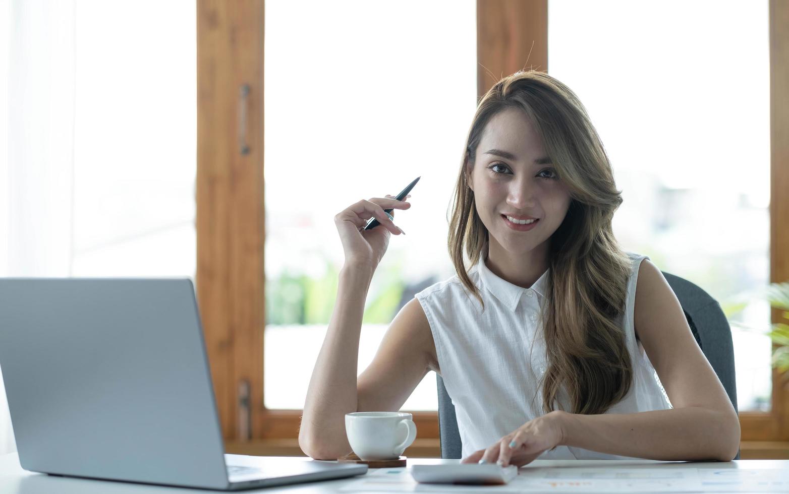 Charming Asian businesswoman working with a laptop at the office. Looking at camera. photo