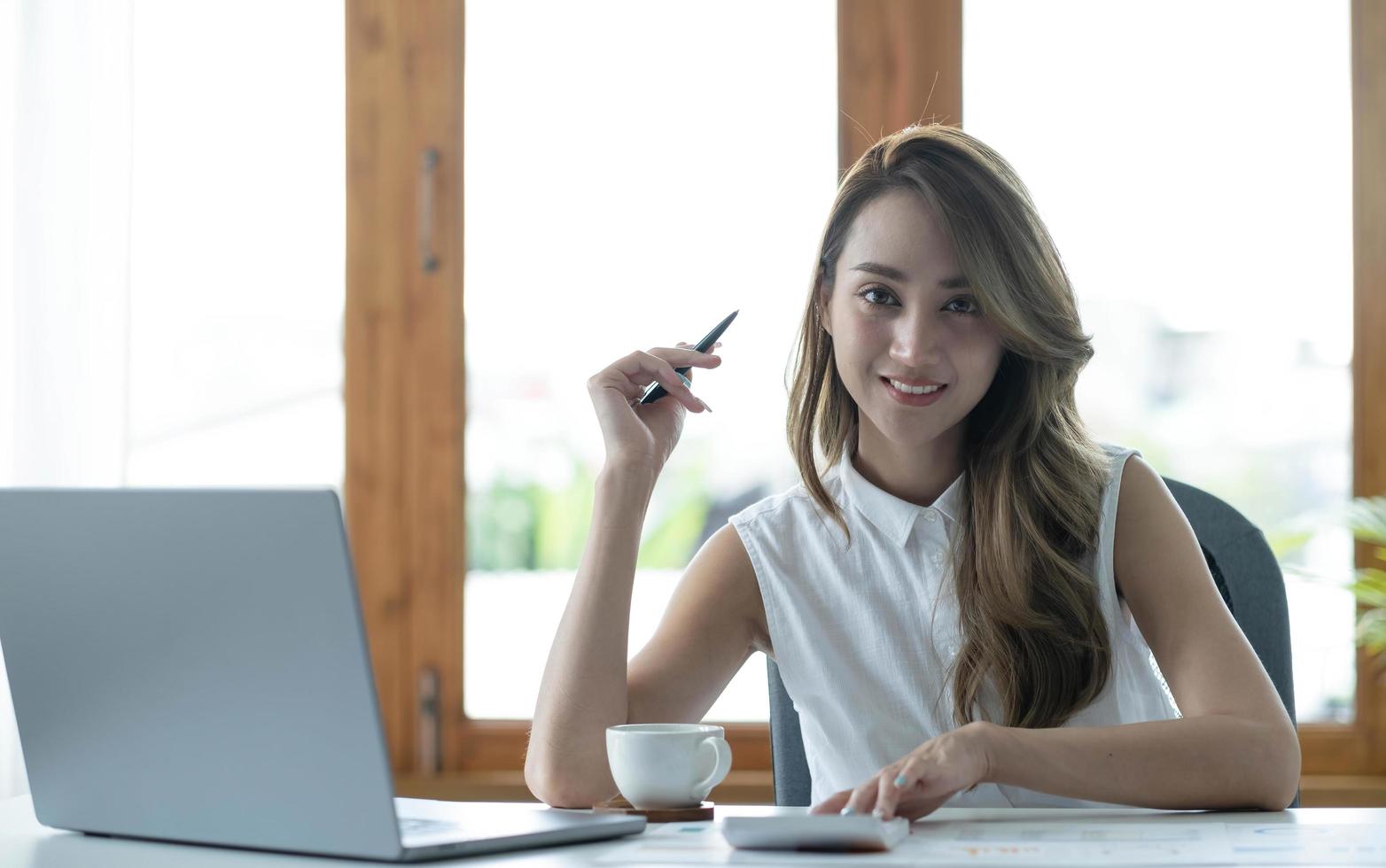 encantadora mujer de negocios asiática que trabaja con una computadora portátil en la oficina. mirando a la cámara. foto