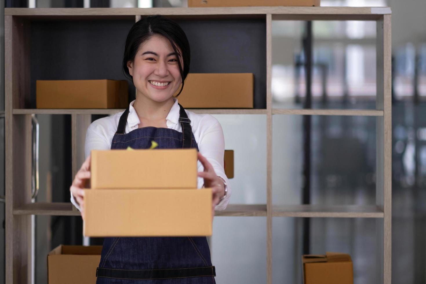 Startup small business entrepreneur of freelance Asian woman using a laptop with box Cheerful success Asian woman her hand lifts up online marketing packaging box and delivery SME idea concept photo