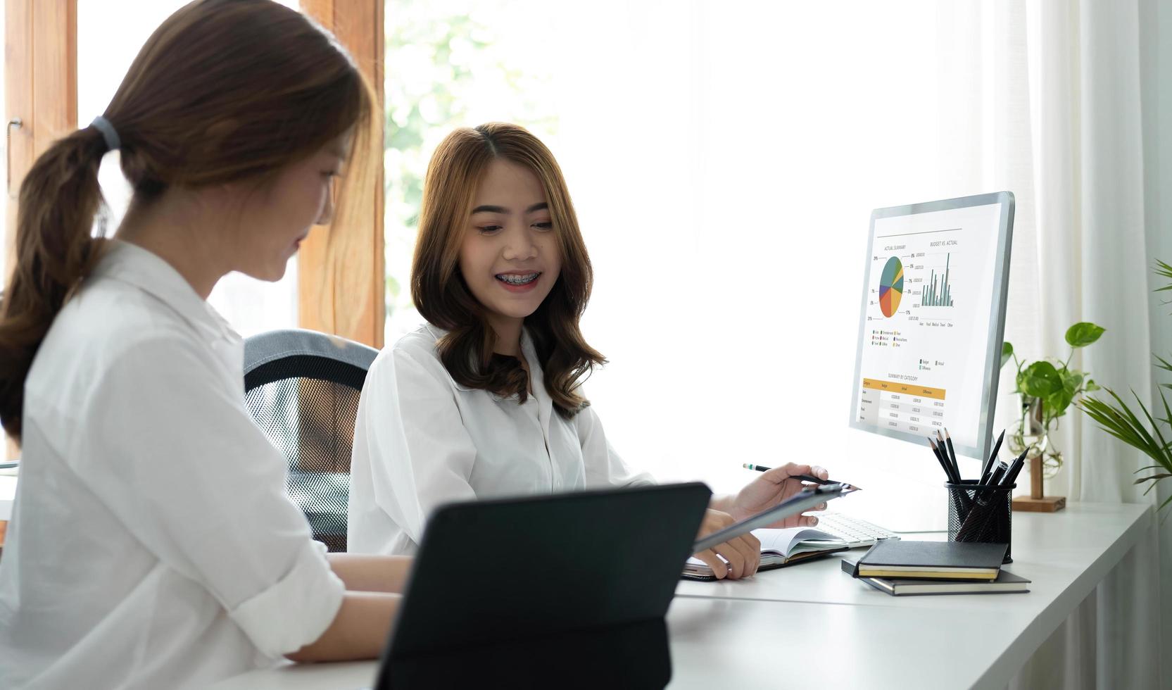 Two young Asian businesswoman discuss investment project working and planning strategy. Business people talking together with laptop computer at office. photo