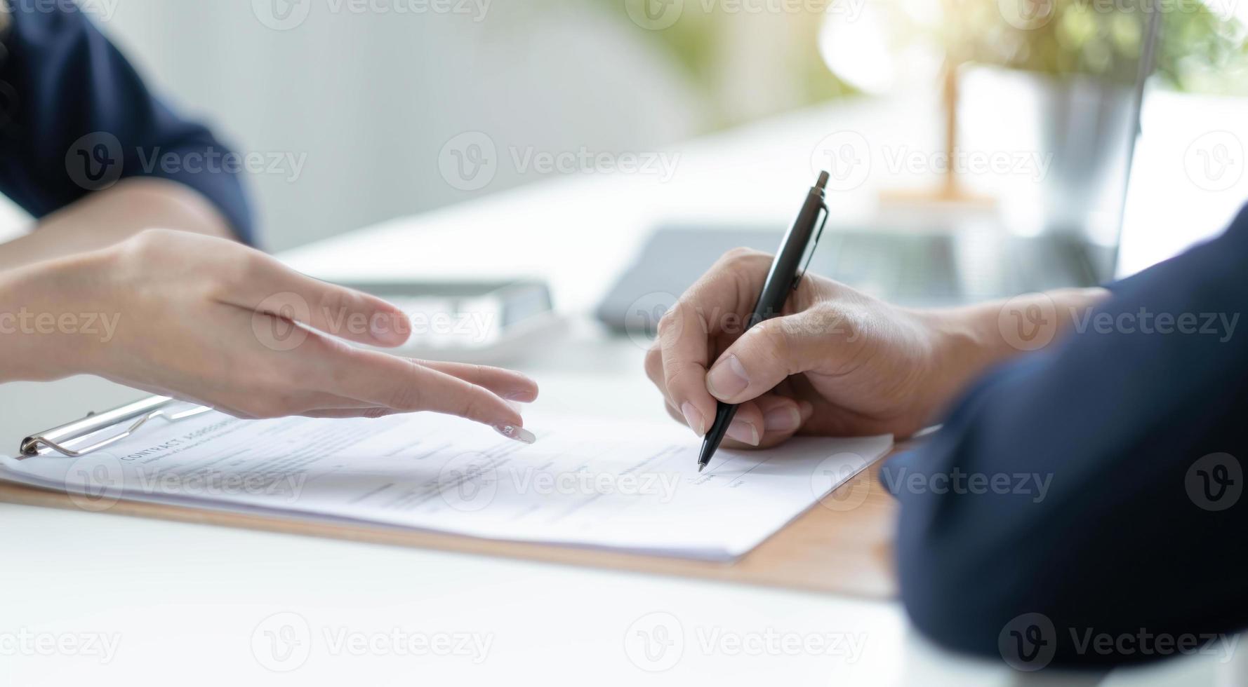 primer plano de la mano de una paciente anciana firmando un contrato de seguro médico en el consultorio médico. médico femenino muestra el lugar del cliente jubilado para poner la firma en la política de cobertura de atención médica foto