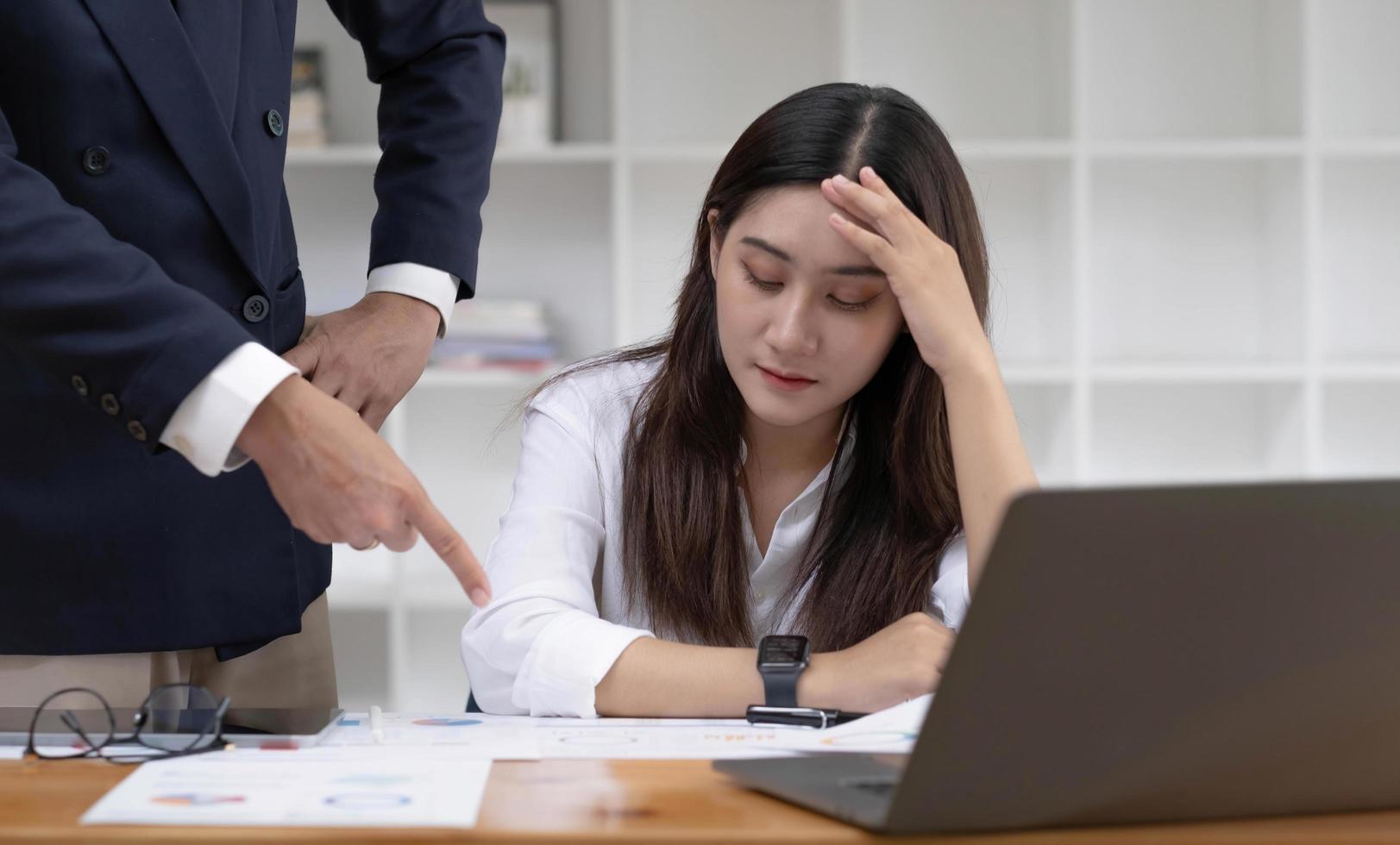 Tired and bored young Asian businesswoman or female office worker getting a complain from her male boss in the office about her work performance. photo