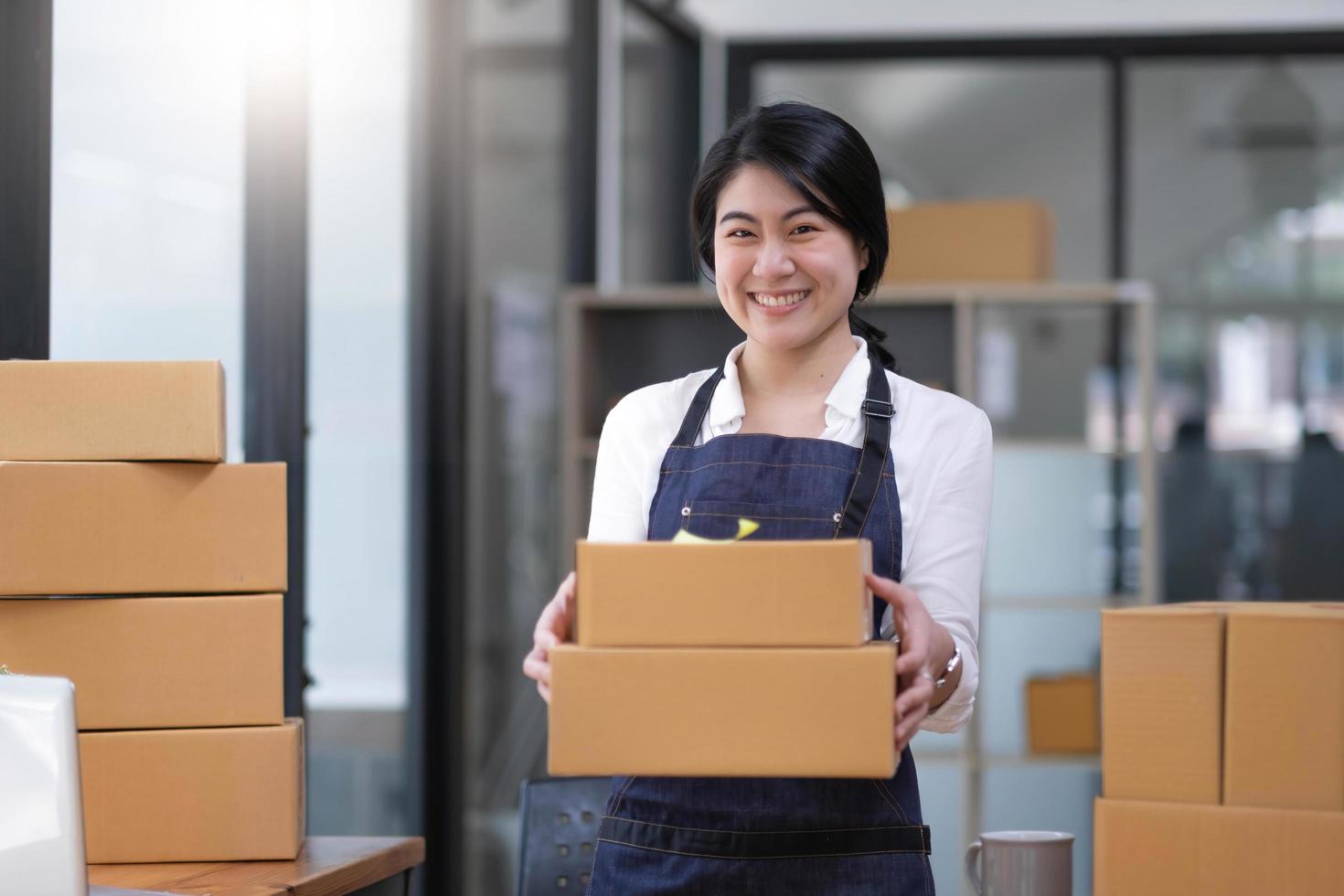 Startup small business entrepreneur of freelance Asian woman using a laptop with box Cheerful success Asian woman her hand lifts up online marketing packaging box and delivery SME idea concept photo