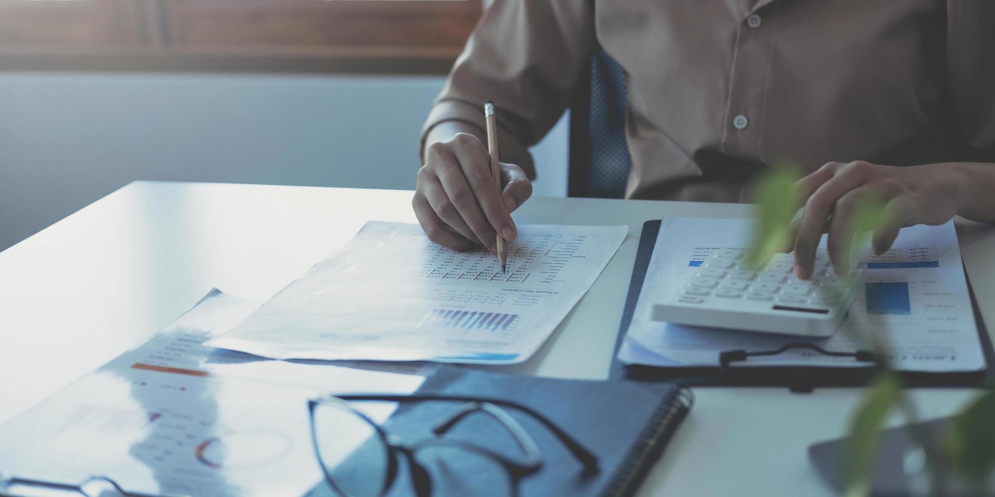 mujer de negocios usando calculadora y escribiendo nota con cálculo. mujer que trabaja en la oficina con computadora portátil y documentos en su escritorio foto