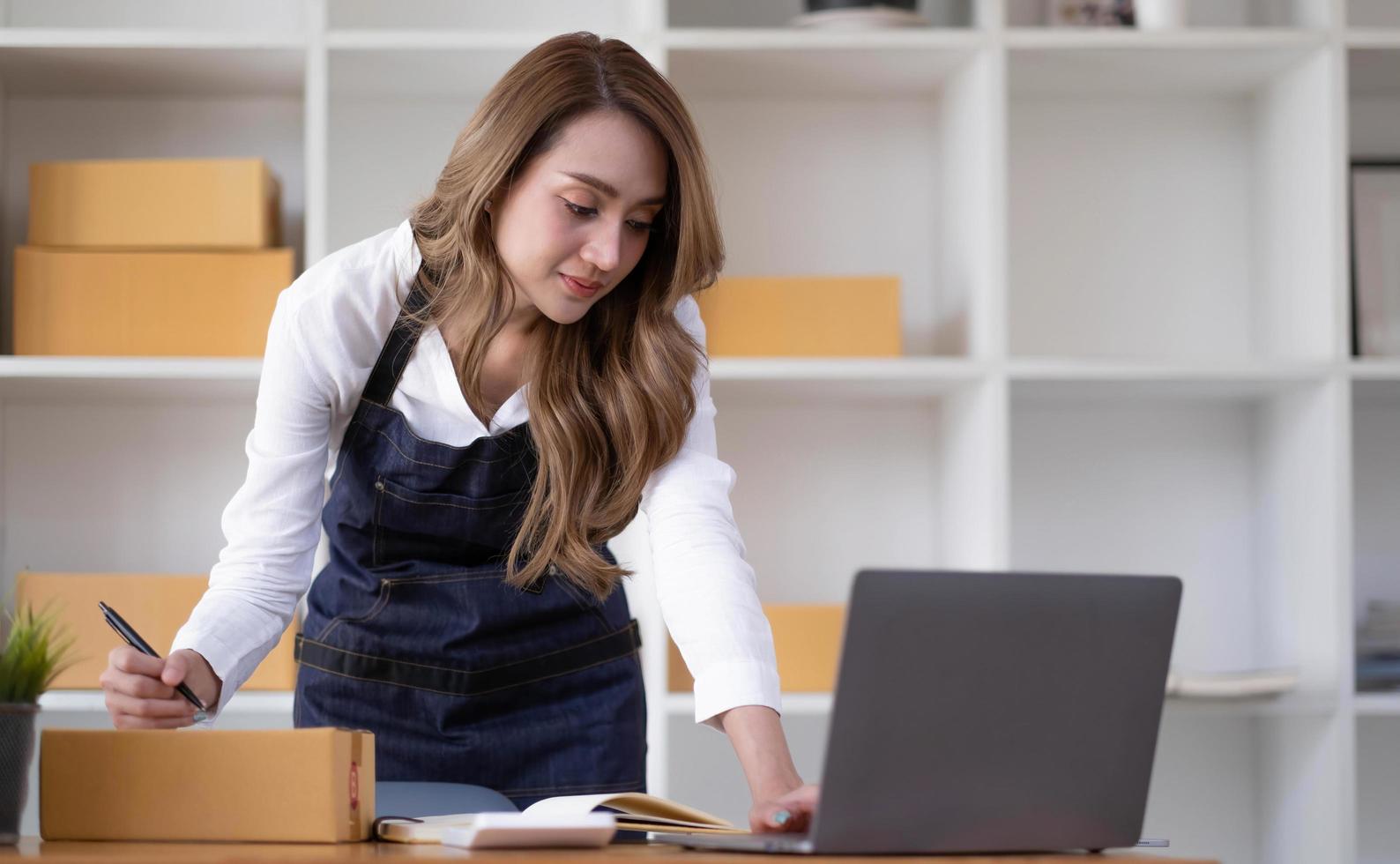 startup sme pequeña empresaria sme o mujer asiática independiente que usa una computadora portátil con caja, joven mujer asiática de éxito con su mano levantada, caja de embalaje de marketing en línea y entrega, concepto sme. foto