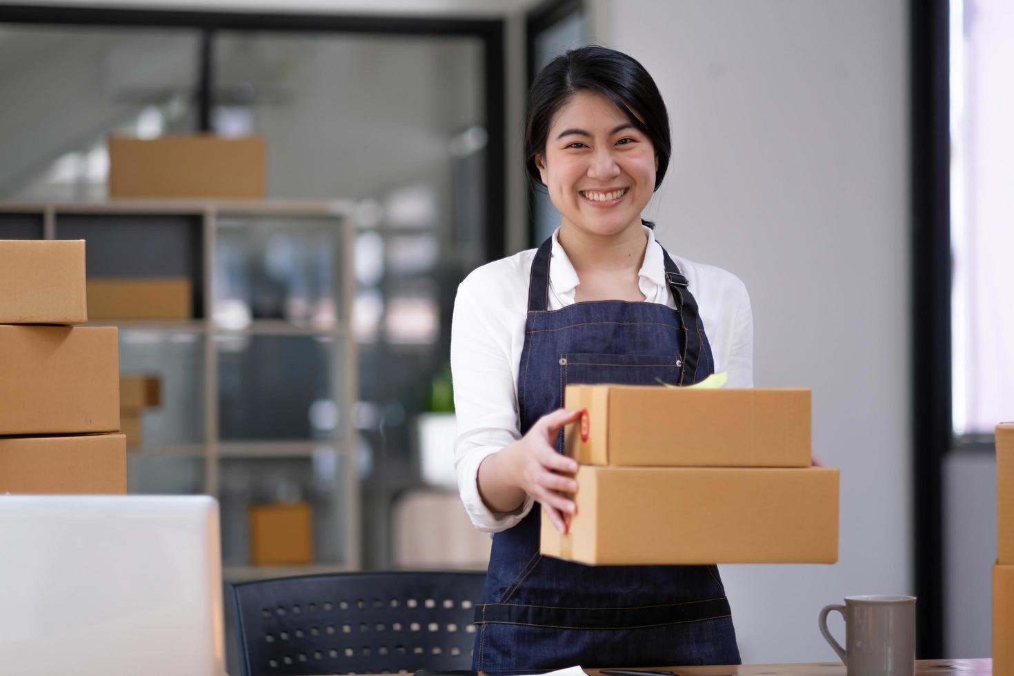 Startup small business entrepreneur of freelance Asian woman using a laptop with box Cheerful success Asian woman her hand lifts up online marketing packaging box and delivery SME idea concept photo