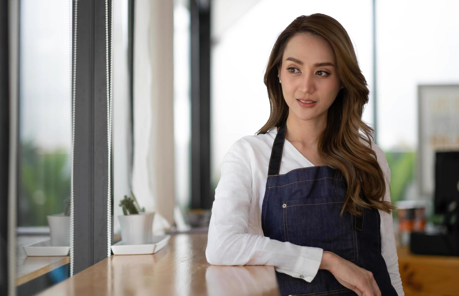 abriendo una pequeña empresa, una mujer asiática feliz en un delantal de pie cerca de una cafetería, propietaria de una pequeña empresa, restaurante, barista, café, en línea, pyme, empresario y concepto de vendedor foto