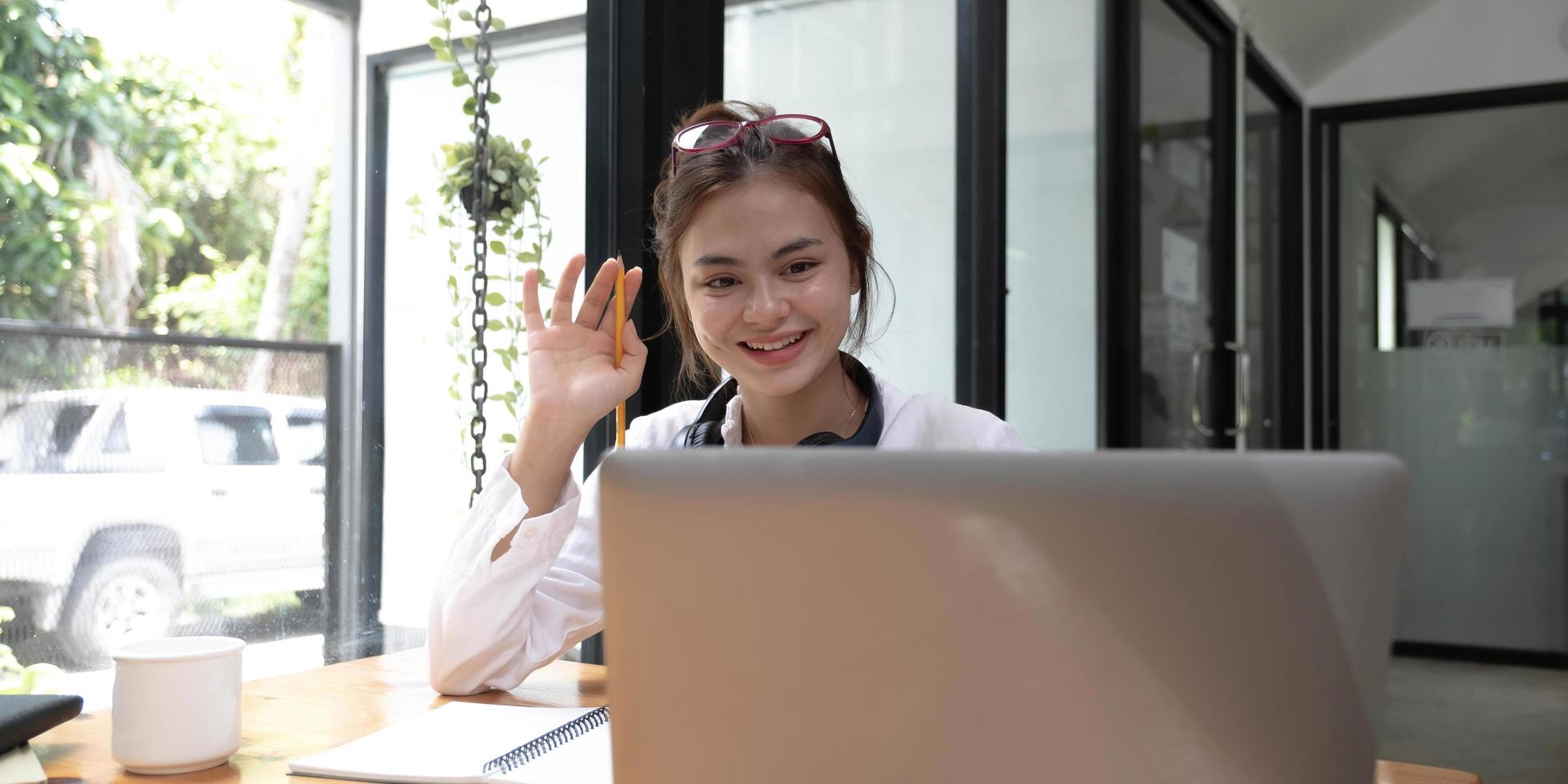 Happy young asian teen girl sit on sofa at home holding phone looking at screen waving hand video calling distance friend online in mobile chat app using smartphone videochat application. photo