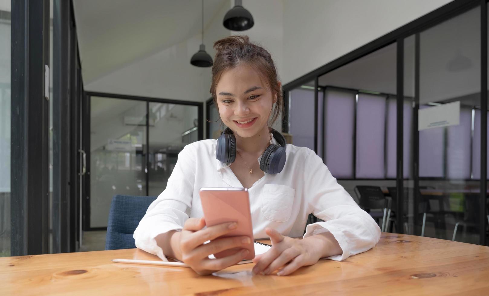 Happy young asian teen girl sit on sofa at home holding phone looking at screen waving hand video calling distance friend online in mobile chat app using smartphone videochat application. photo