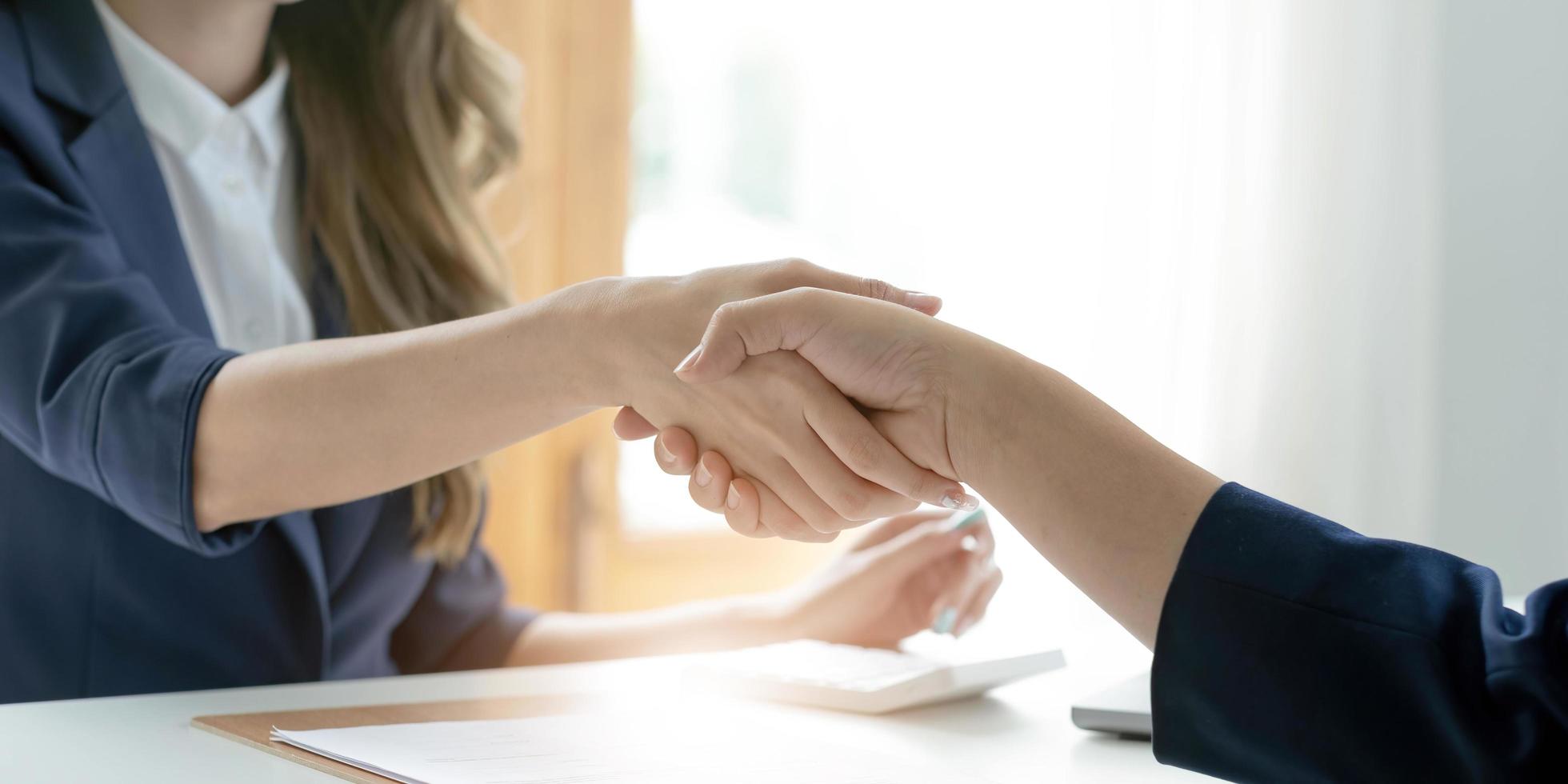 Closeup of unrecognizable happy businesswoman shaking hands with business partner after signing contract during meeting in office. photo